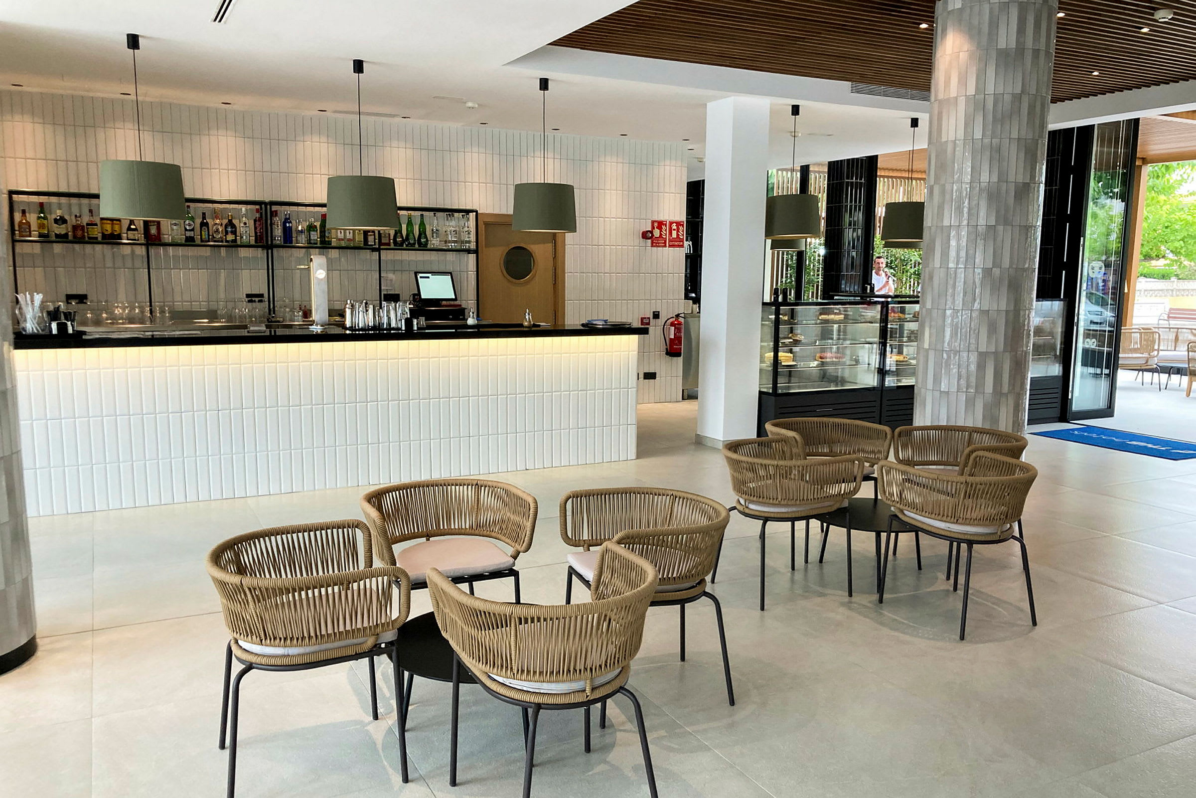 Bild av en modern lounge med en bar, bord och stolar samt en glasmonter med bakverk. (AI-genererad text)