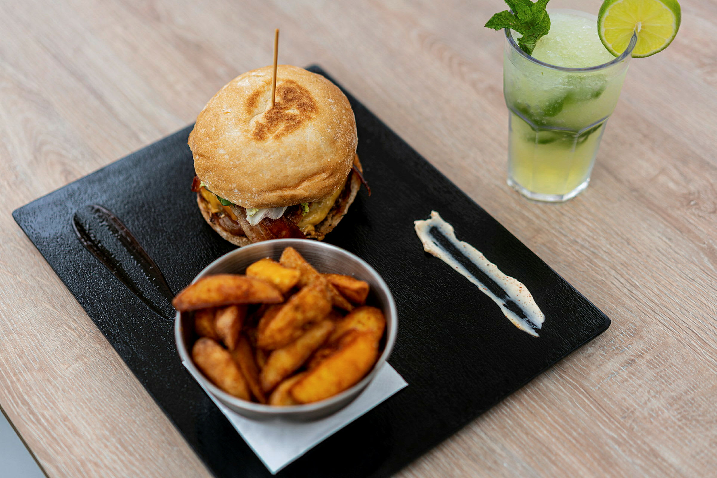 En matuppsättning med en hamburgare, ett fat med klyftpotatis och en svalkande dryck med lime och mynta. (AI-genererad text)