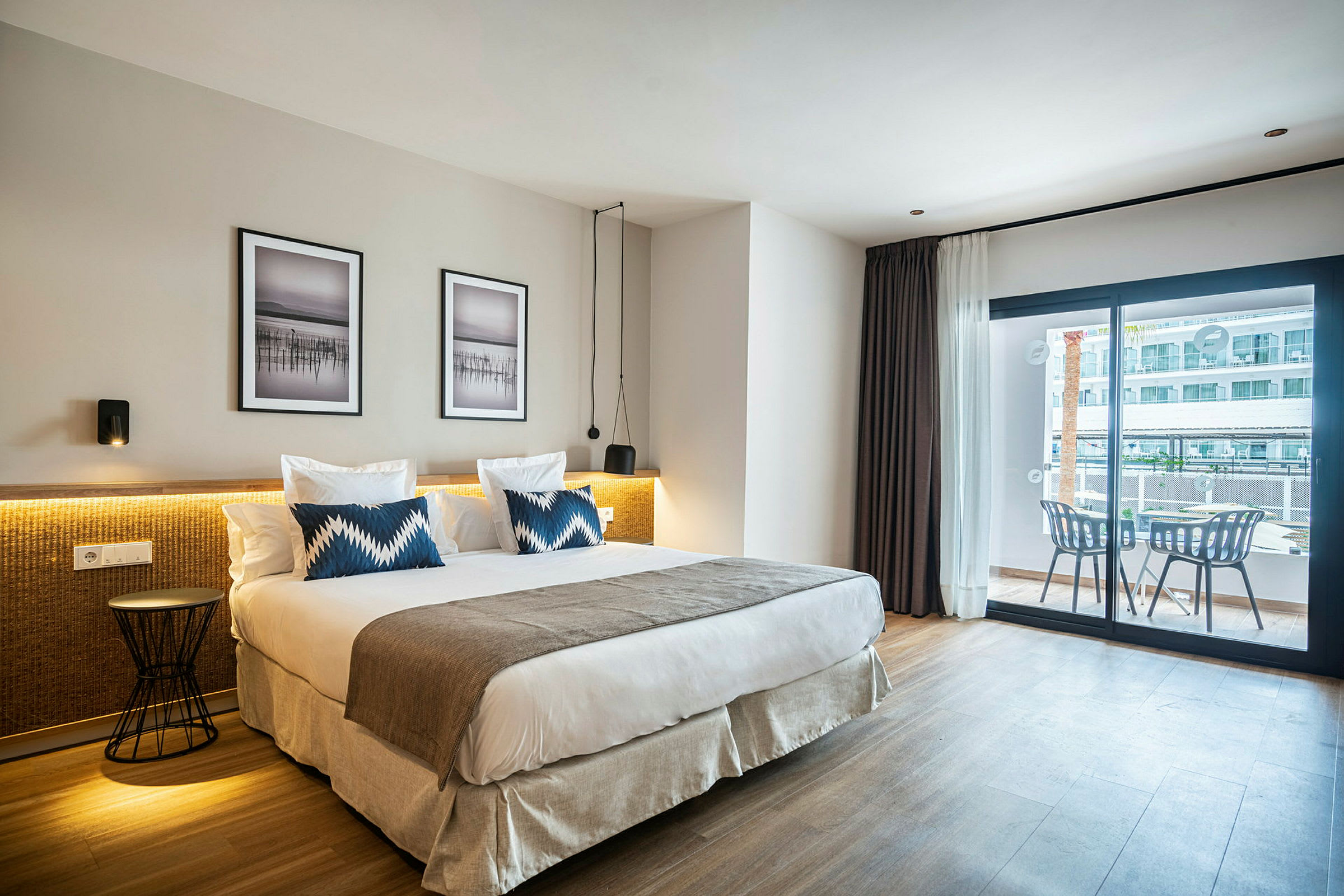 Hotellrum med en stor säng, två kuddar och modern inredning, samt en balkong med sittmöbler. (AI-genererad text)