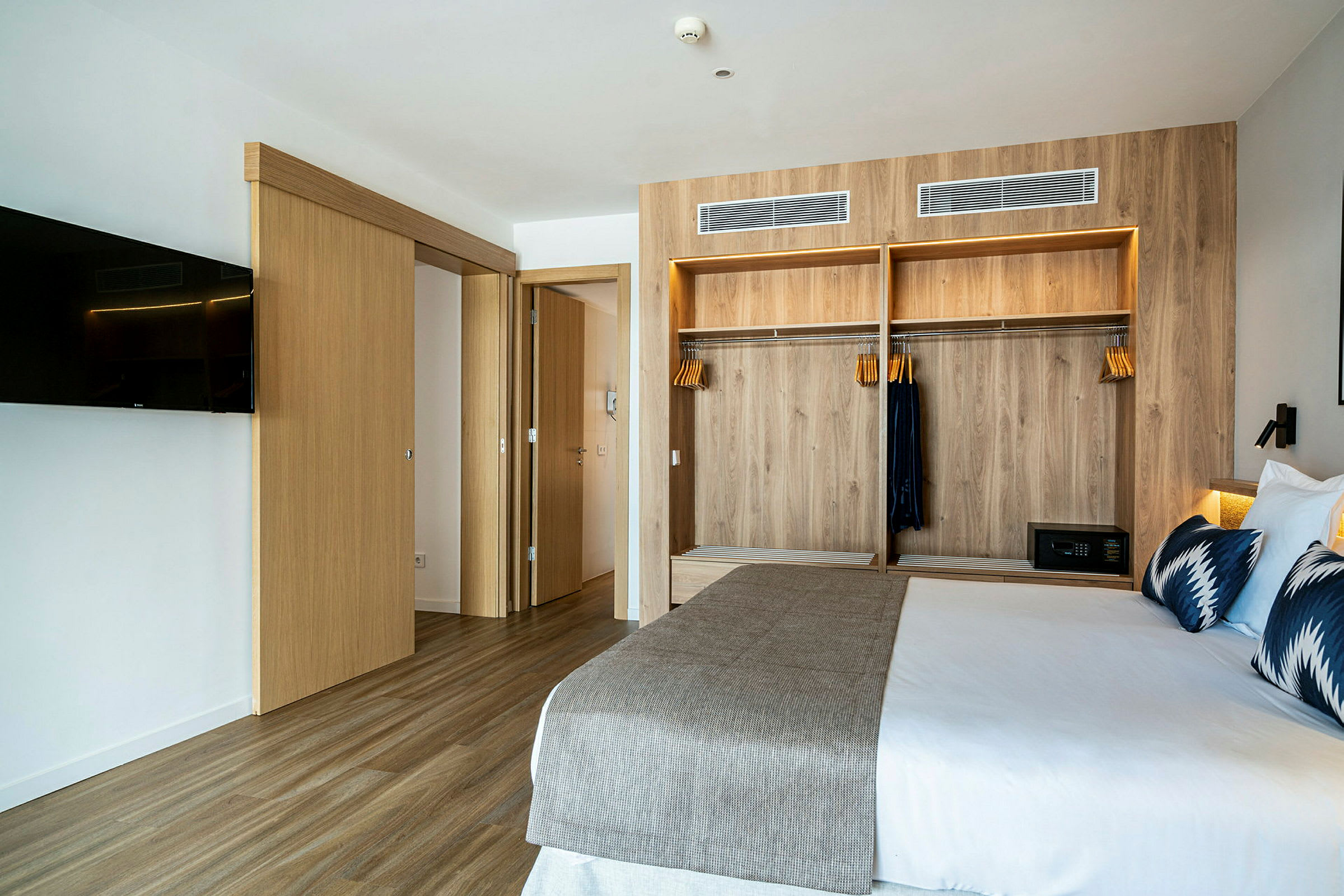 Ett modernt hotellrum med en säng, en träbeklädd garderob och en väggmonterad TV. (AI-genererad text)