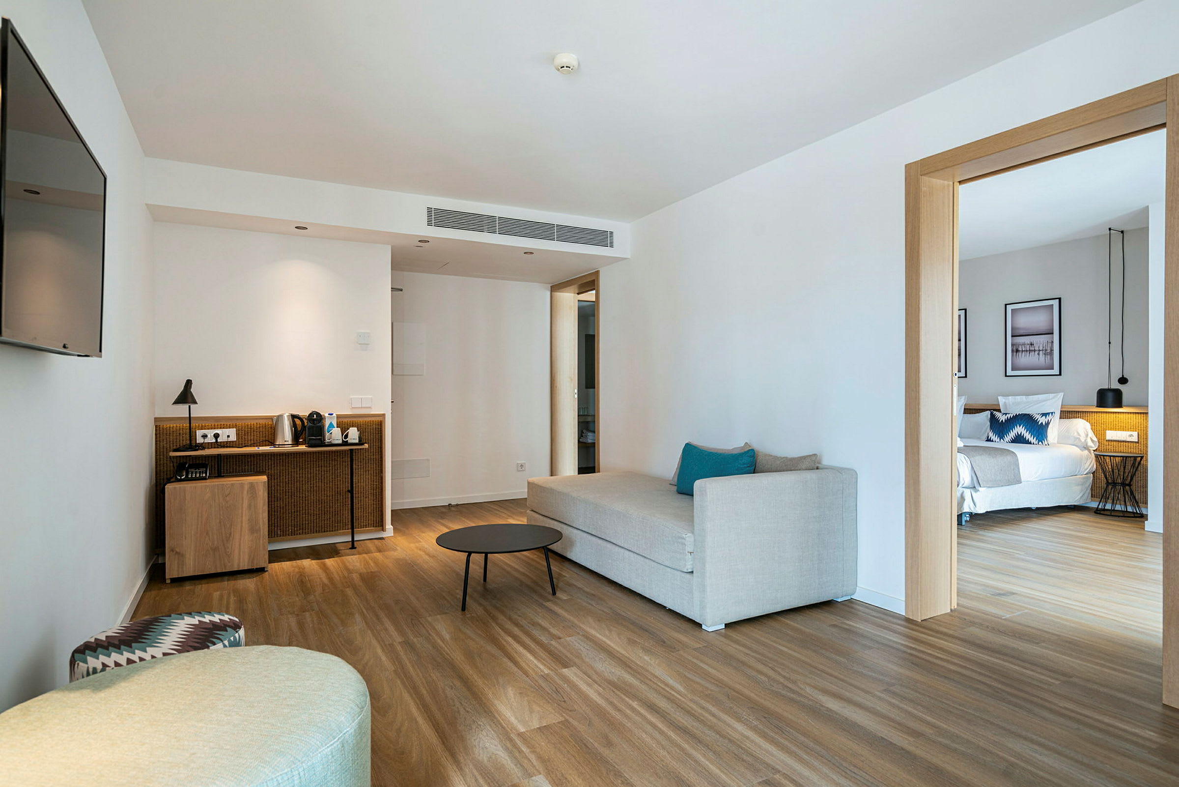 Ett hotellrum med ett vardagsrum utrustat med en soffa och soffbord, samt ett delvis synligt sovrum med en säng. (AI-genererad text)