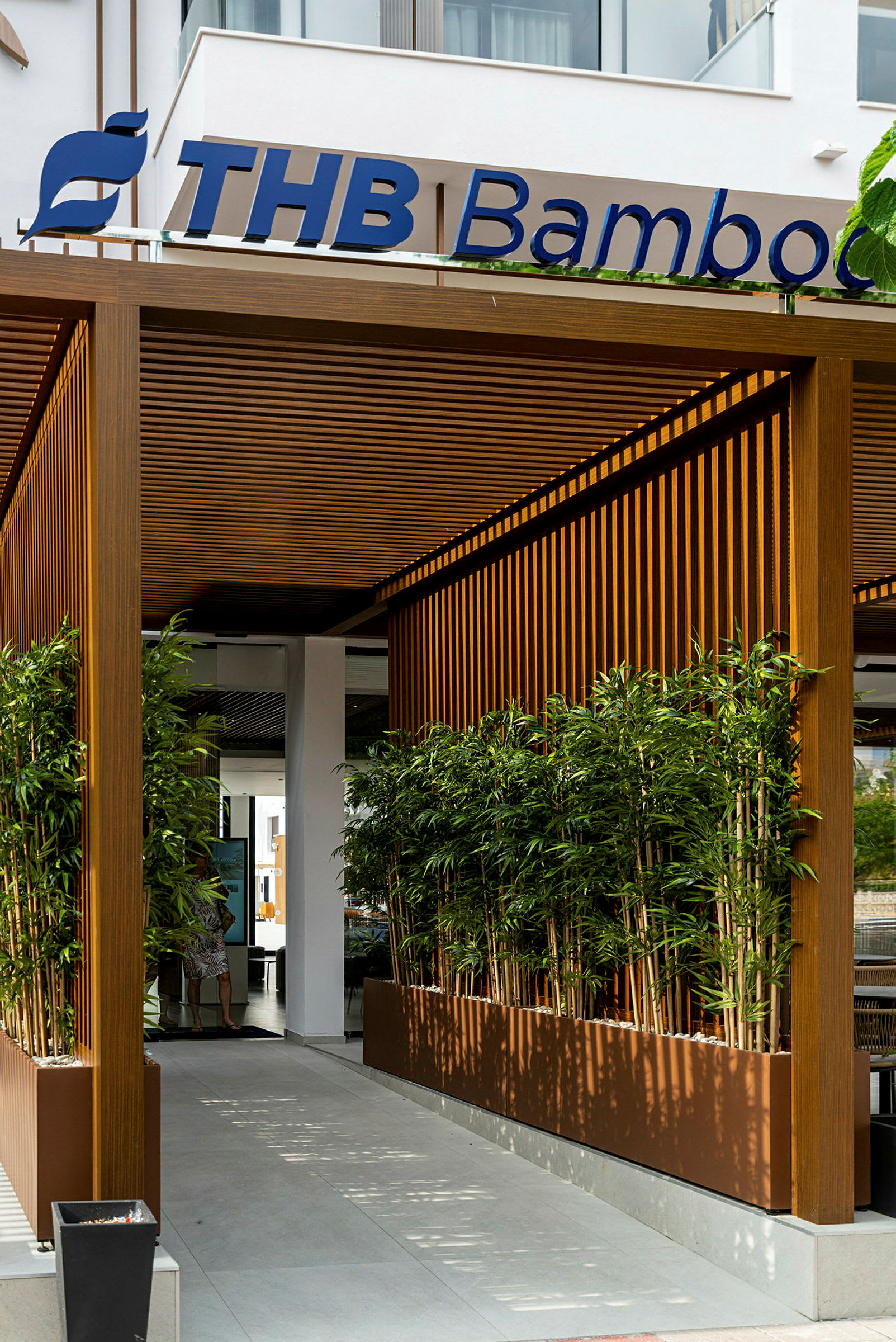 Entrén till en byggnad med en träpergola, omgiven av bambuplanteringar. (AI-genererad text)