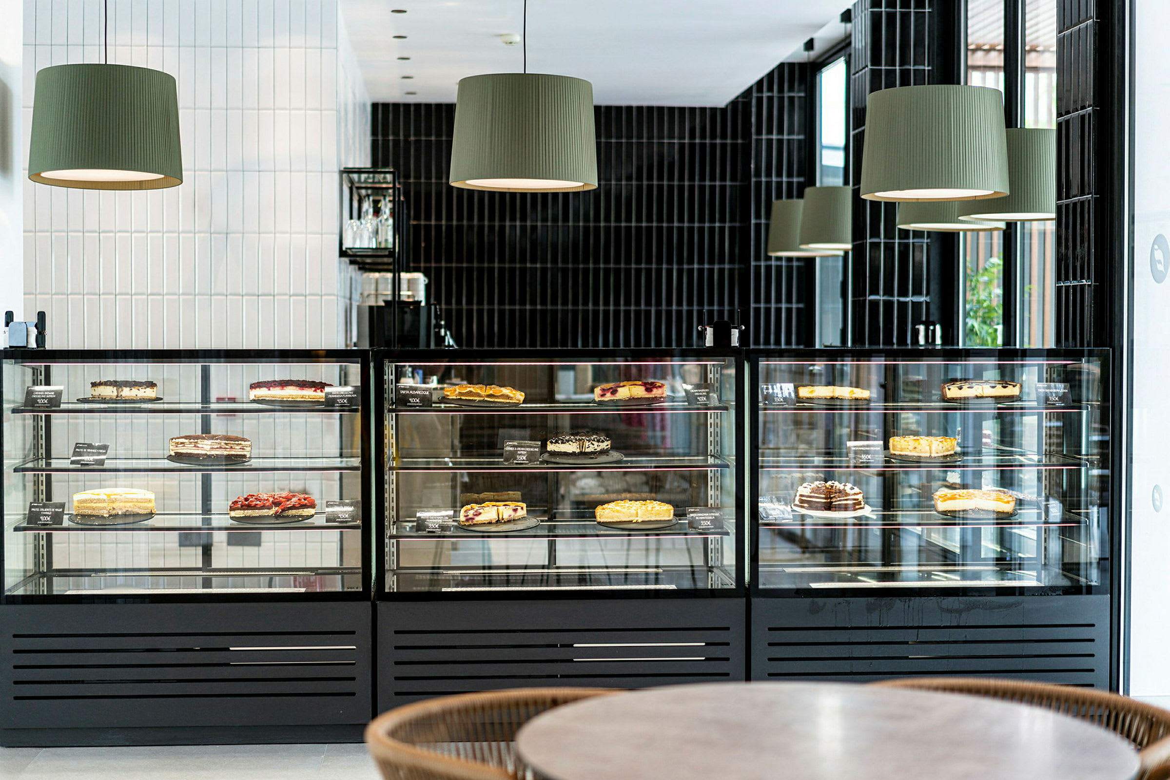 En glasmonter med olika tårtor som är utställda för försäljning i ett modernt café. (AI-genererad text)
