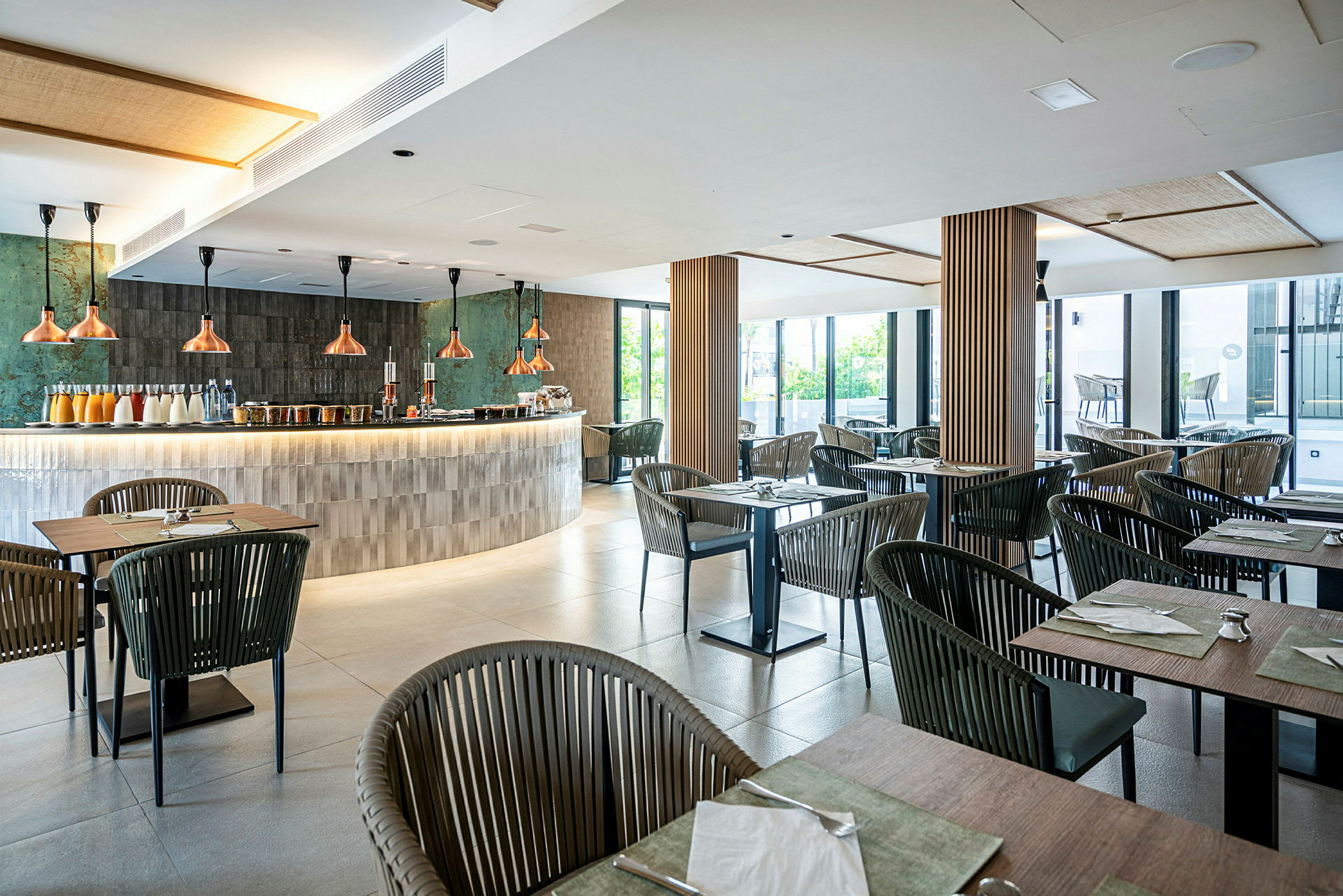 Bild av en modern restaurang med bord och stolar i trä och metall, samt en elegant bardisk med kopparlampor. (AI-genererad text)