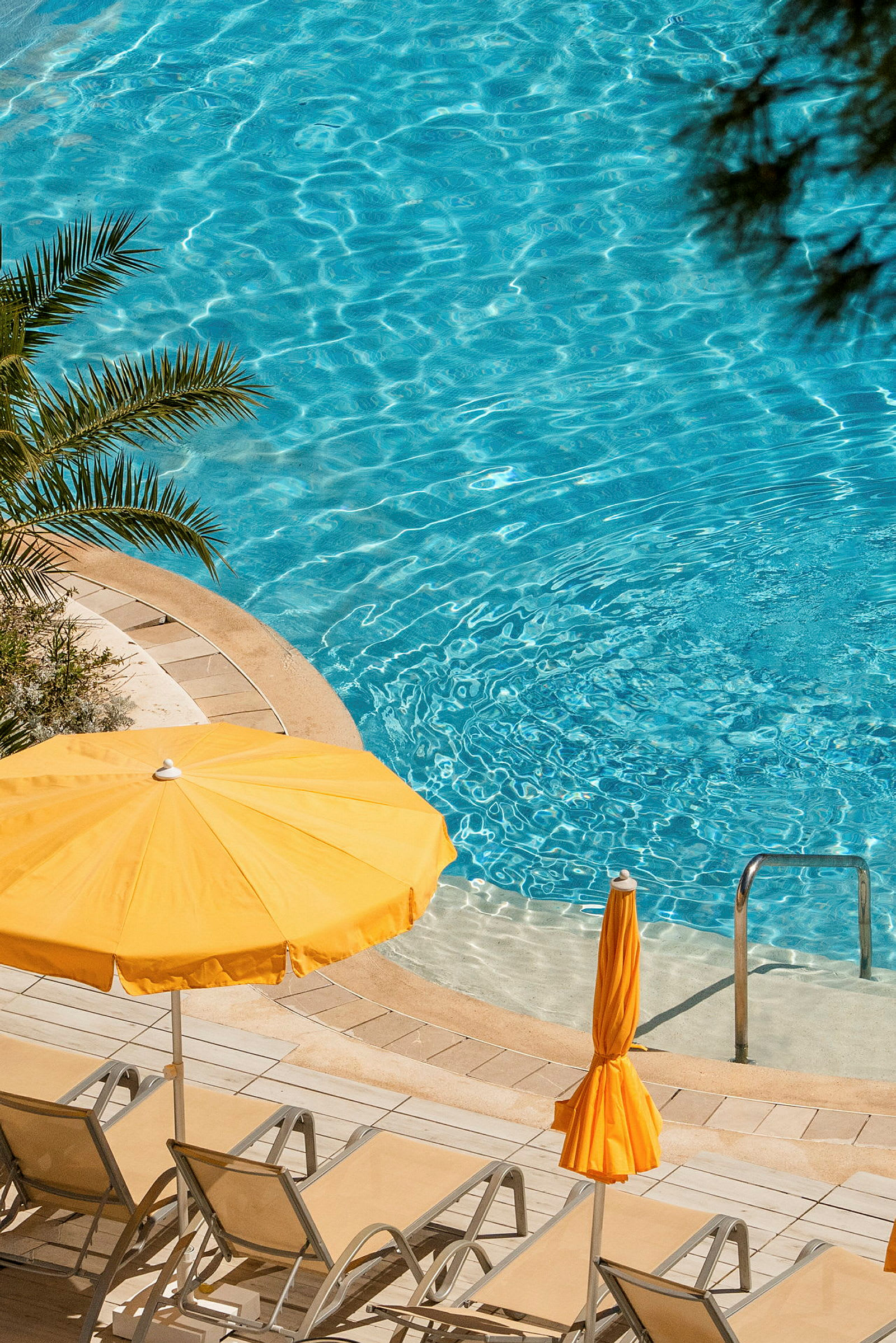 Solstolar och gula parasoller vid en blå pool. (AI-genererad text)
