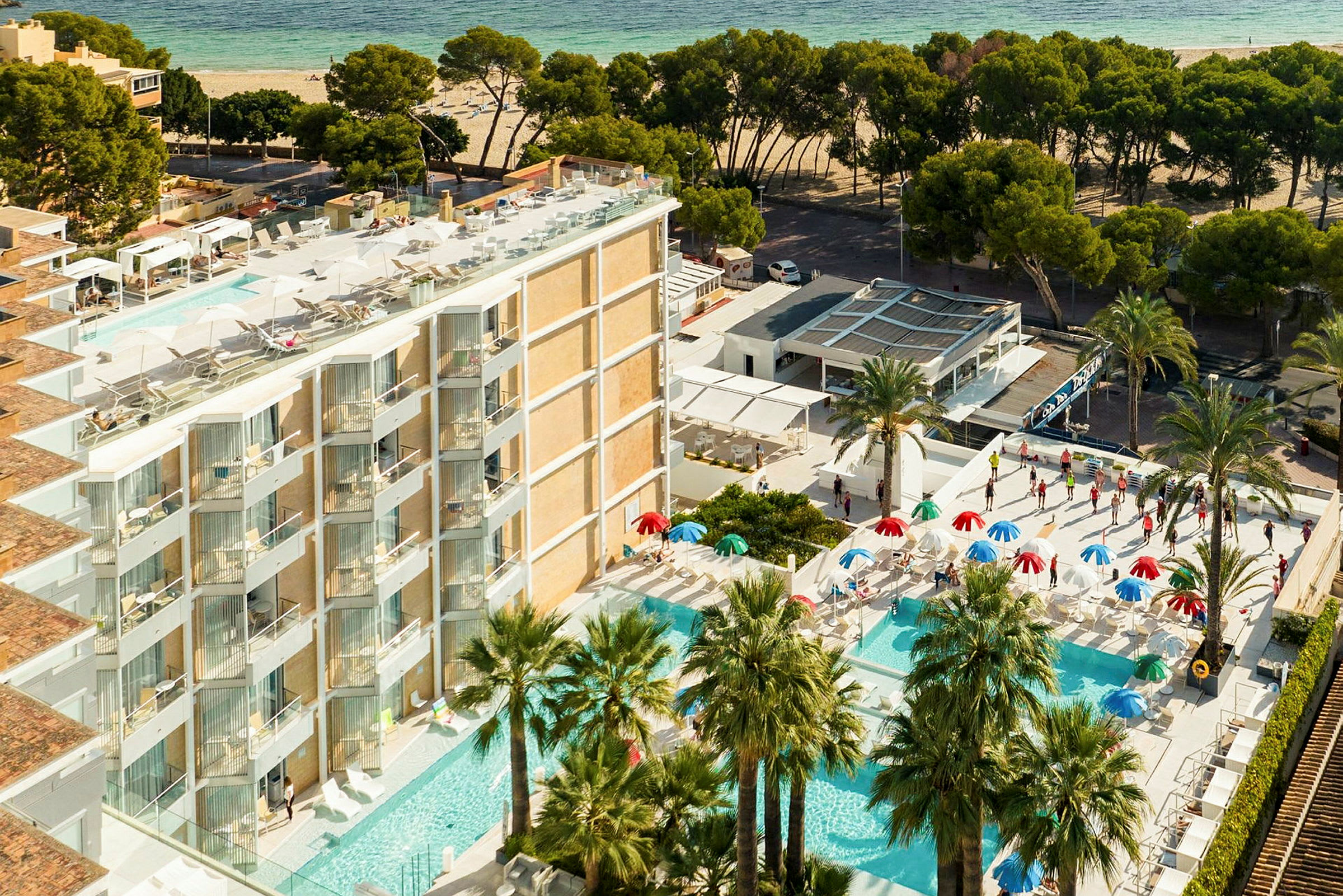 Vy över hotellområde med flera pooler, parasoller och palmer nära en sandstrand. (AI-genererad text)