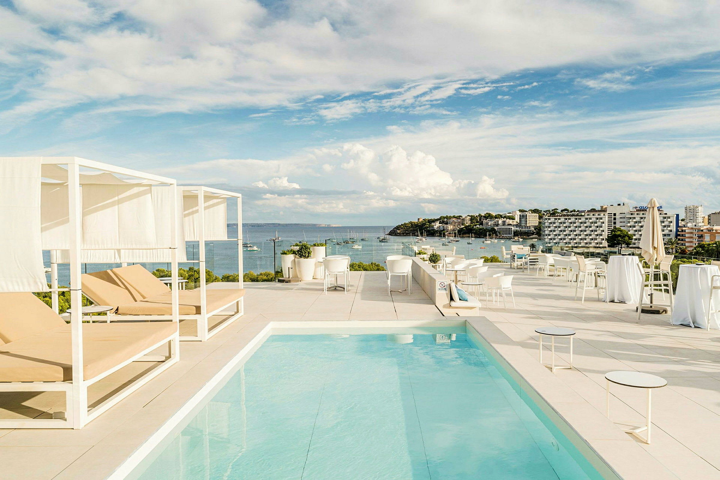 En takterrass med en pool, solstolar och utsikt över havet och en kuststad. (AI-genererad text)