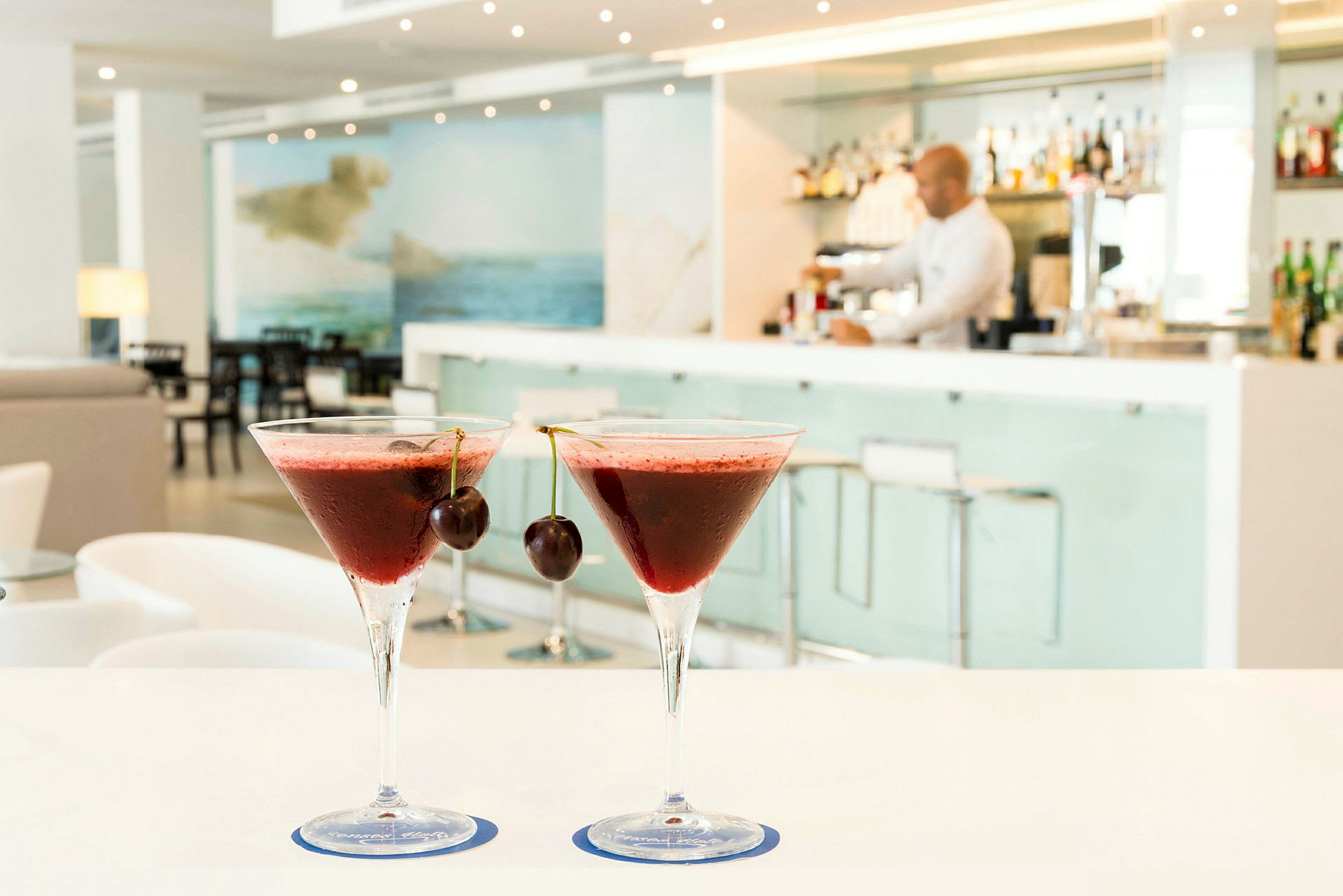 Två röda cocktails med körsbär på toppen står på ett bord i en modern bar. (AI-genererad text)