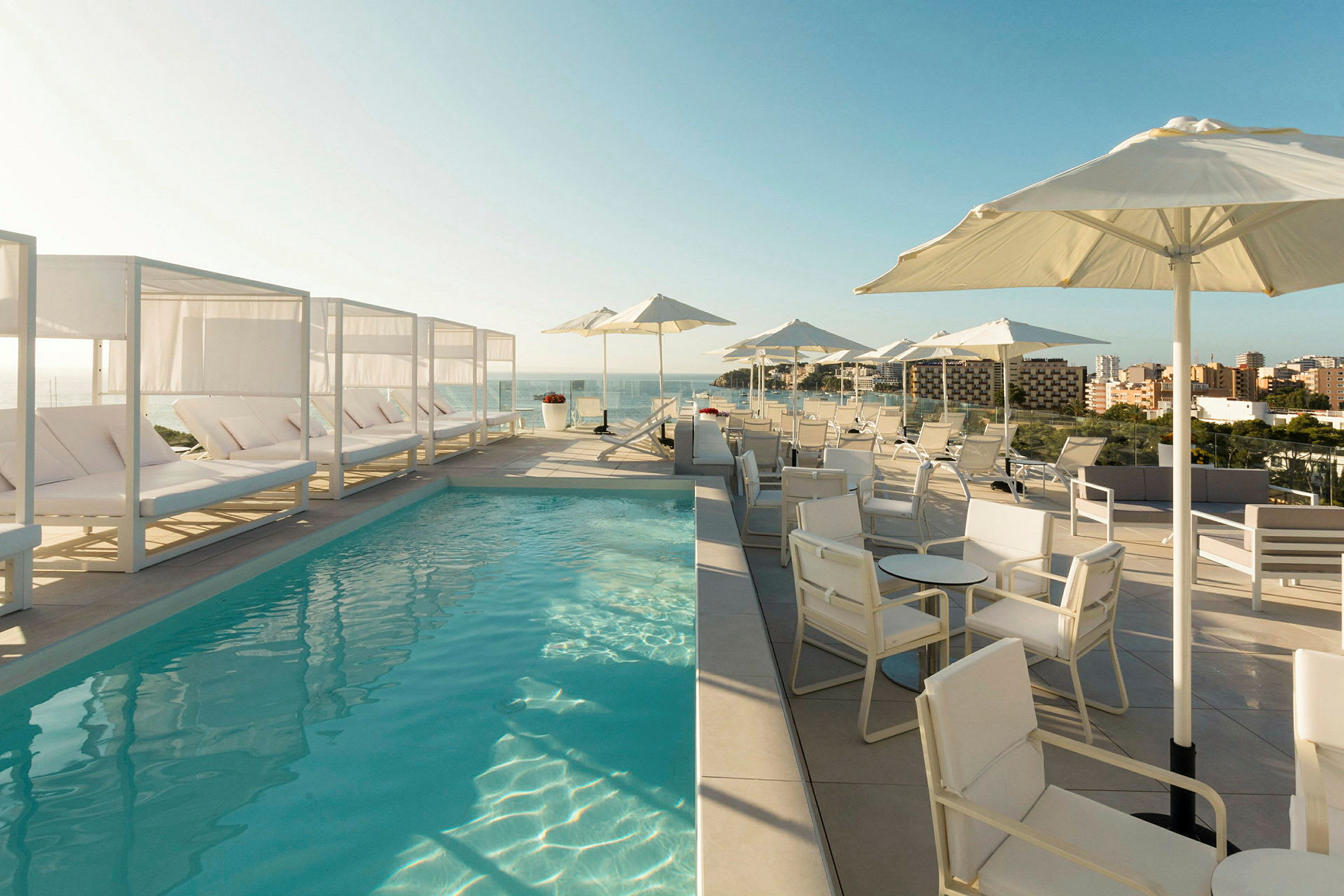 En poolterrass med solstolar, parasoller och utsikt över staden och havet. (AI-genererad text)