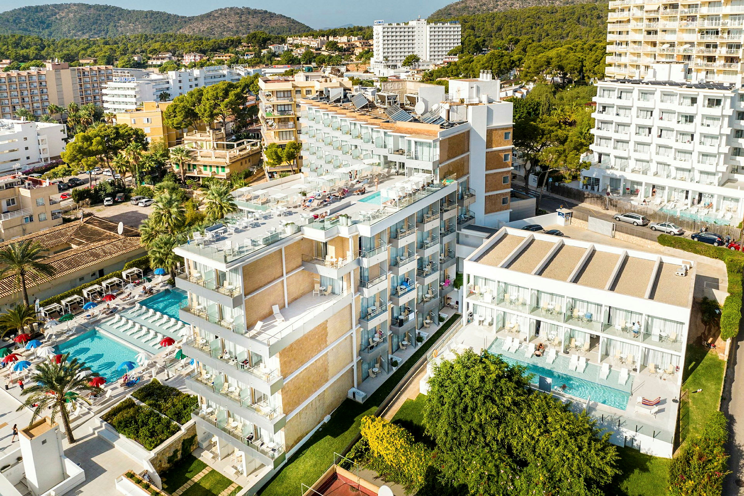 Bild av ett hotellkomplex med poolområde och omgivande byggnader, omgärdat av grönska och kuperad terräng. (AI-genererad text)
