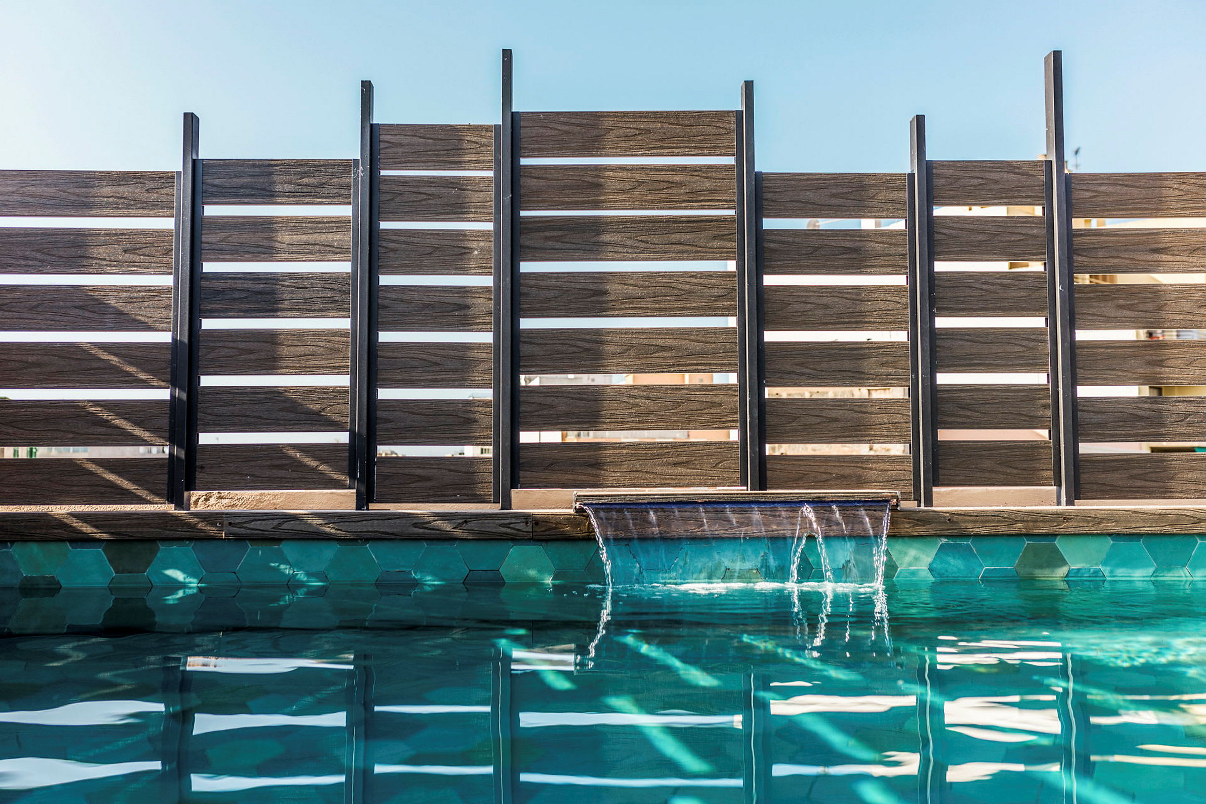 En pool med ett vattenfall och ett trästängsel i bakgrunden. (AI-genererad text)