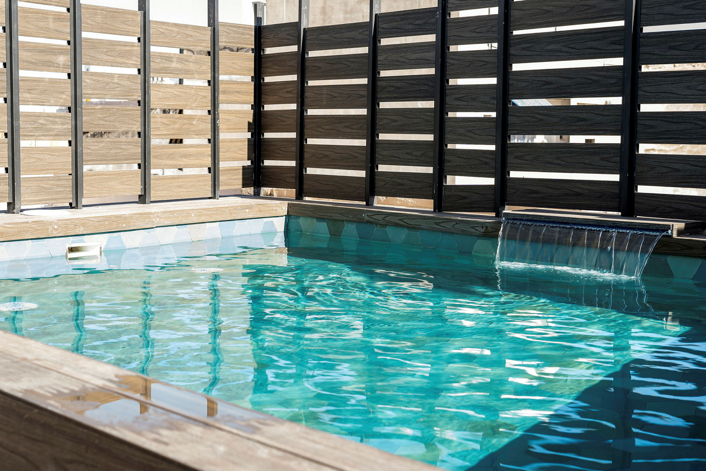 En pool med klart blått vatten och ett vattenfall, omgiven av träpaneler. (AI-genererad text)