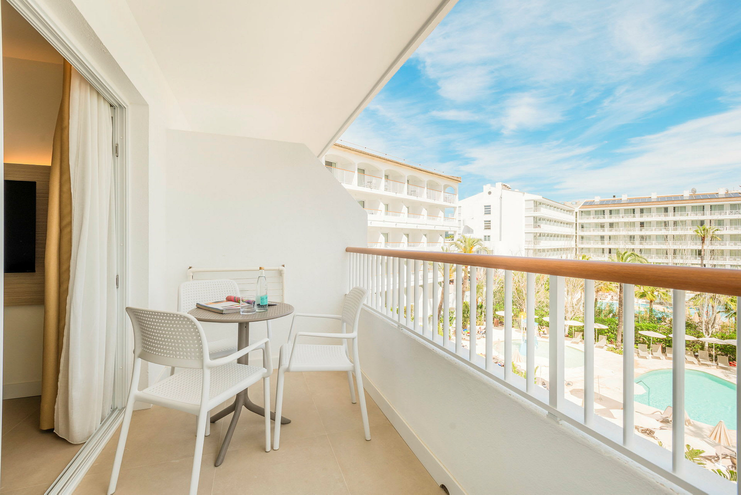 En möblerad balkong med två stolar och ett bord, med utsikt över hotellområde och pool. (AI-genererad text)