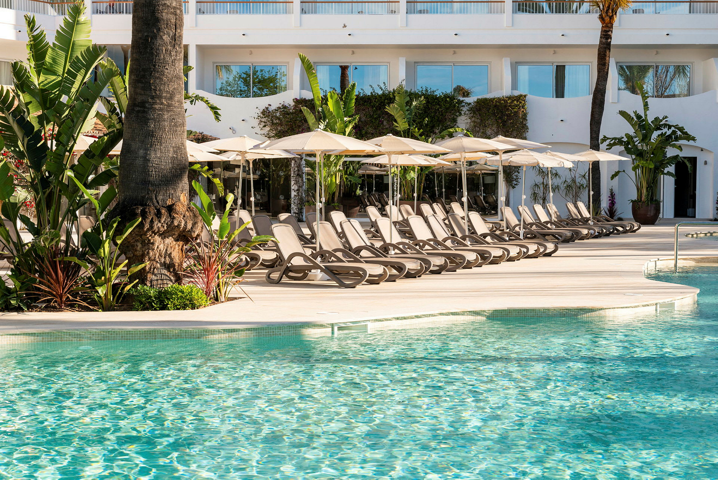 Lokalisering vid swimmingpool med solstolar och parasoller nära en modern byggnad. (AI-genererad text)