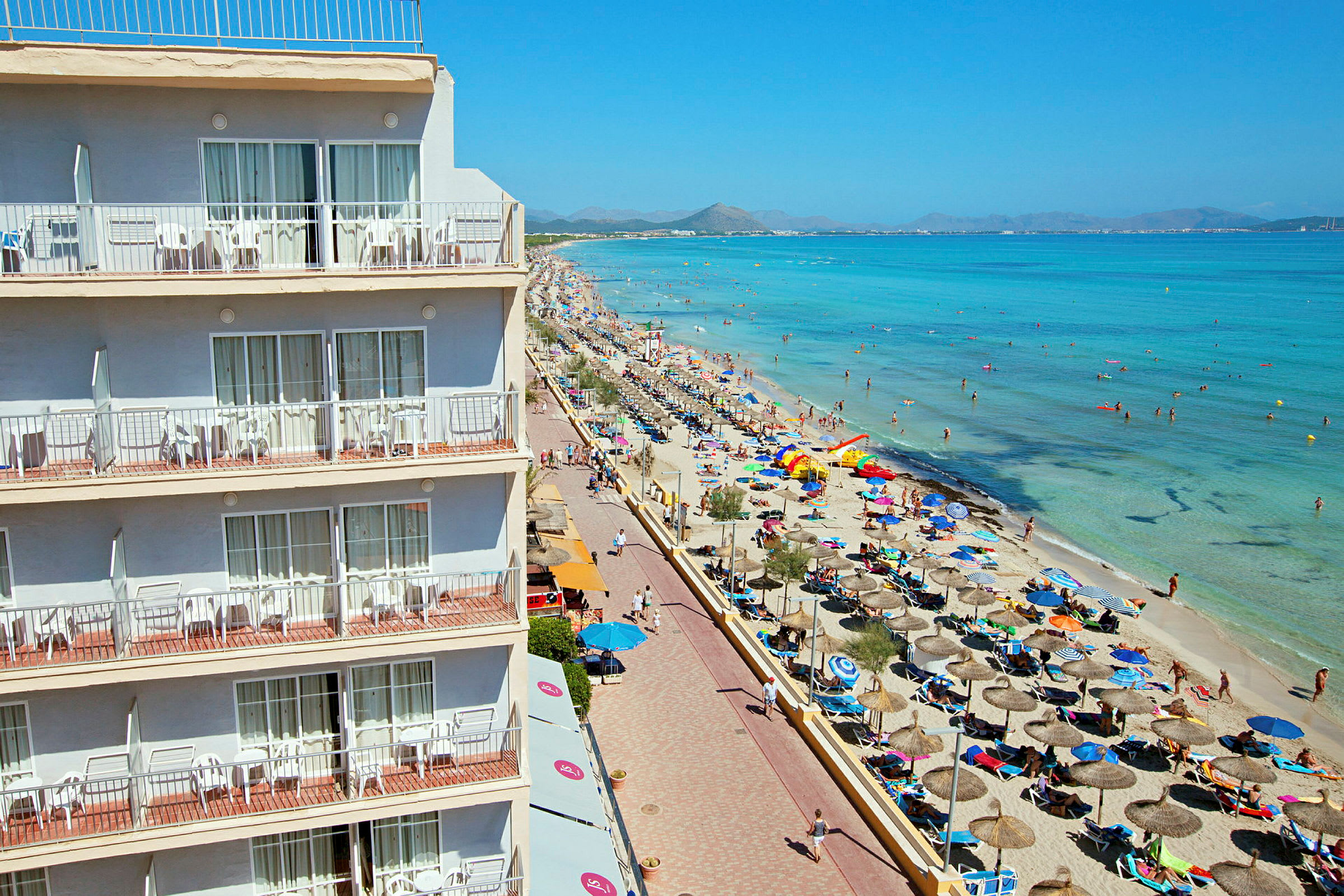 Hotell med balkonger vid en livlig strand och klart hav. (AI-genererad text)