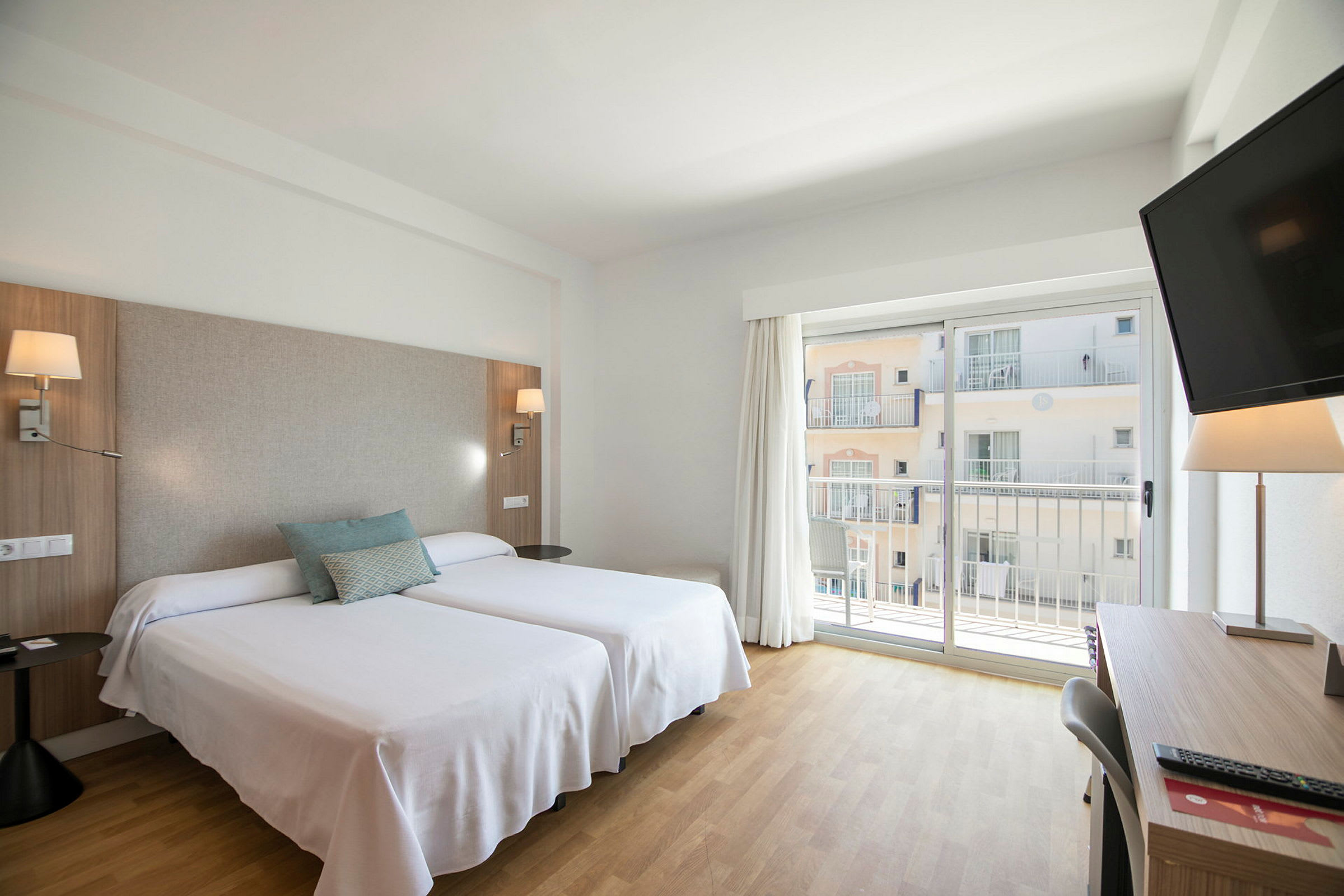 Ett hotellrum med två enkelsängar och balkongdörrar. (AI-genererad text)