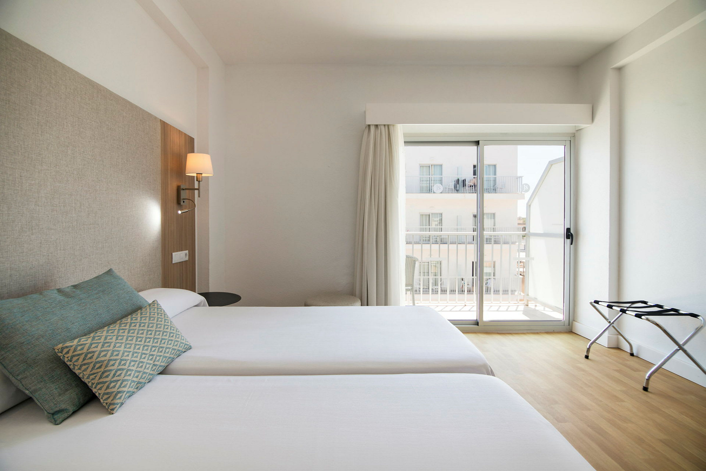 Två enkelsängar i ett hotellrum med ljus inredning och ett fönster med balkong. (AI-genererad text)