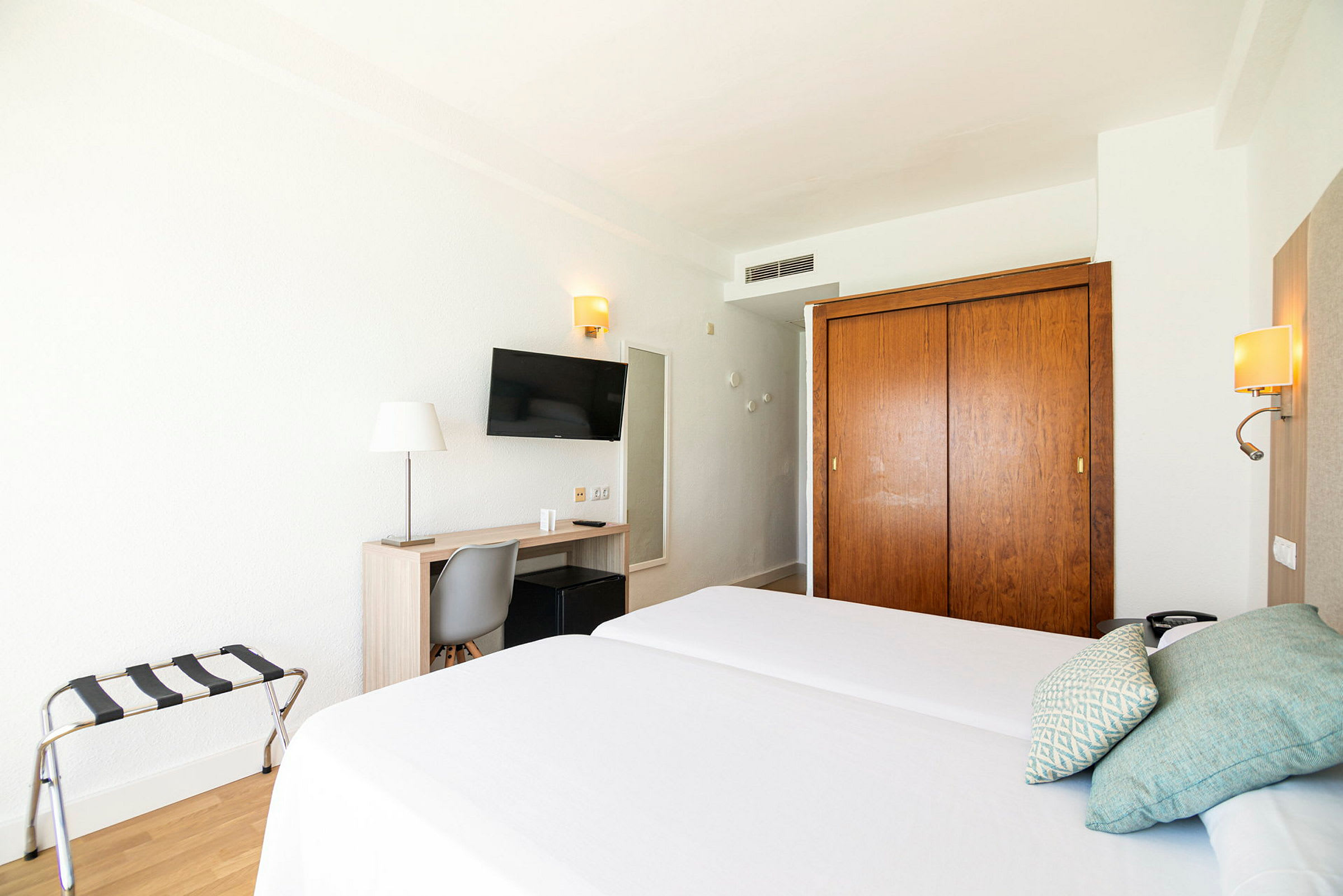 Hotellrum med två enkelsängar, skrivbord, stol, TV och garderob. (AI-genererad text)