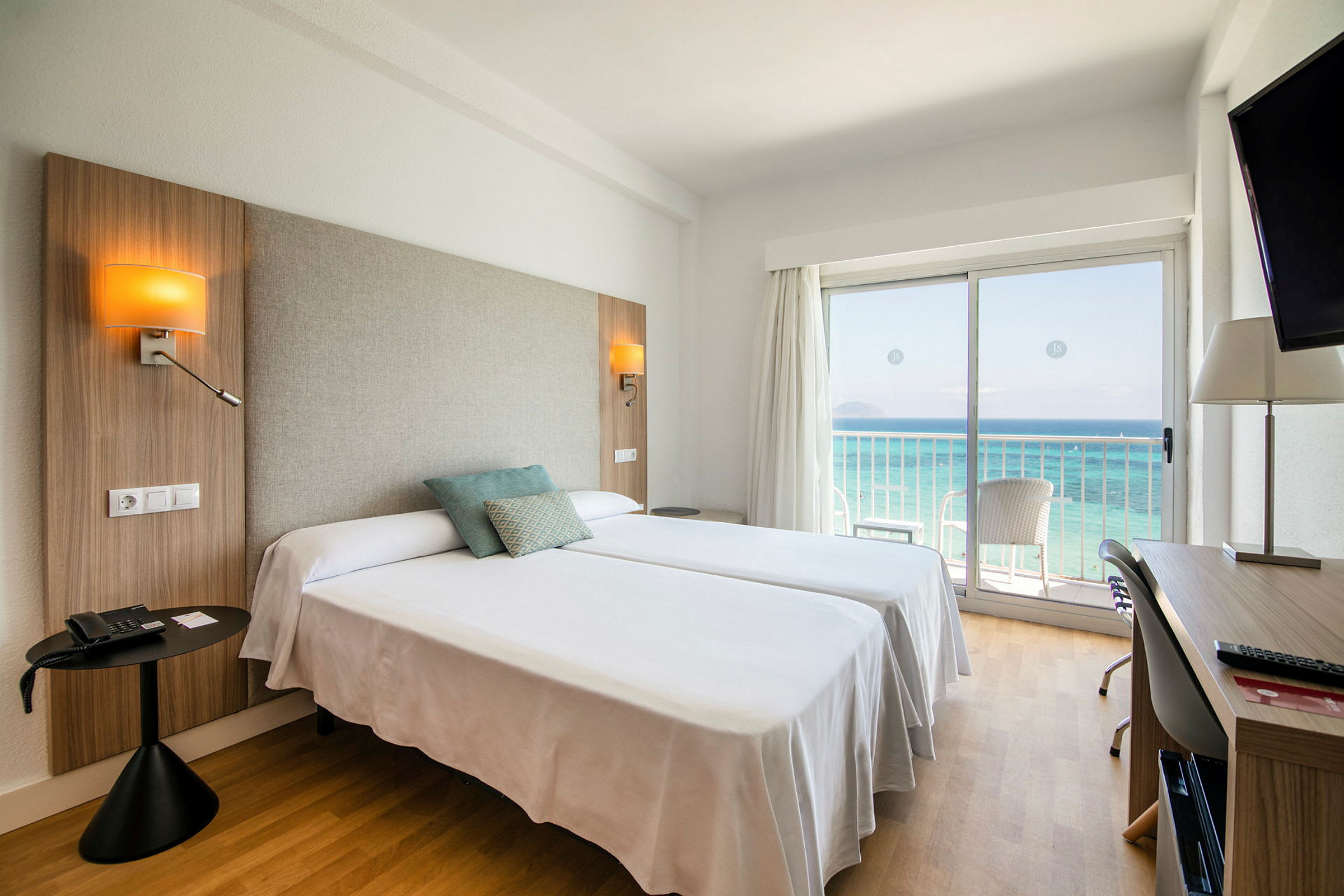 Hotellrum med två sängar, havsutsikt genom en glasdörr och skrivbord. (AI-genererad text)
