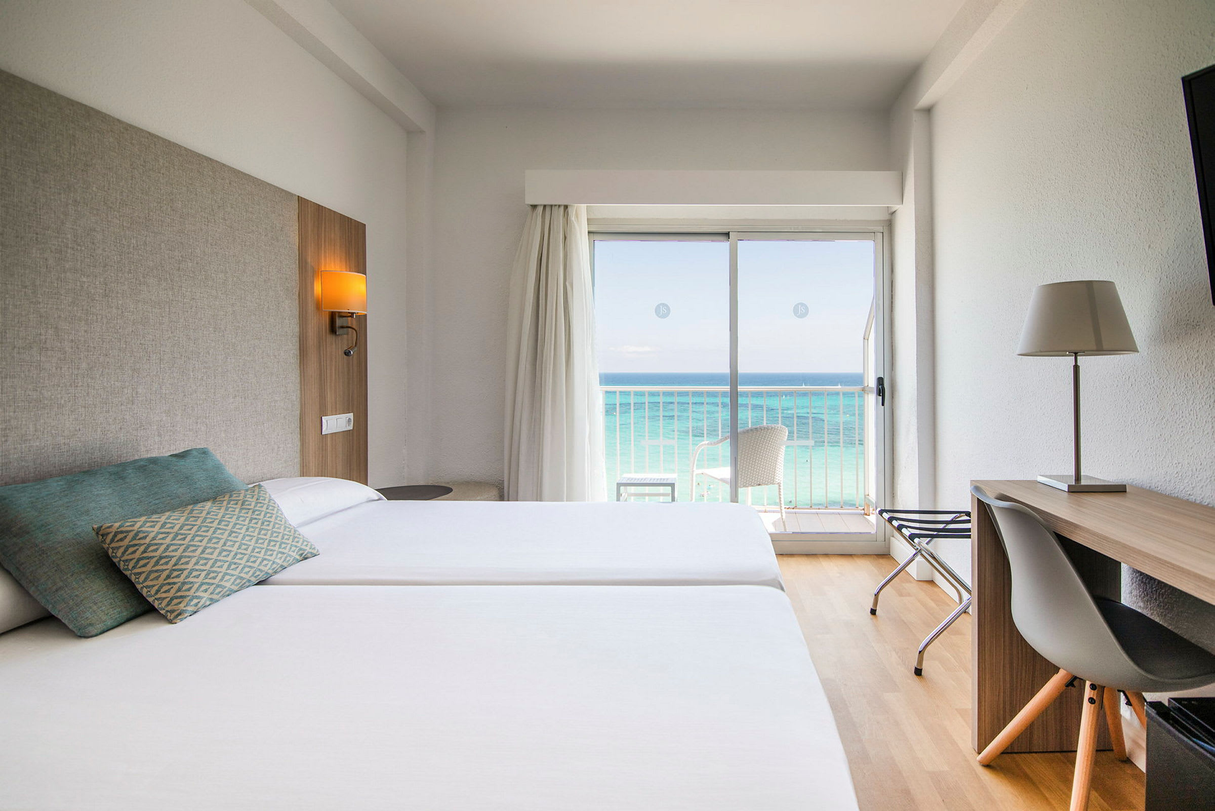 Hotellrum med två sängar, skrivbord och utsikt över havet genom en glasdörr. (AI-genererad text)