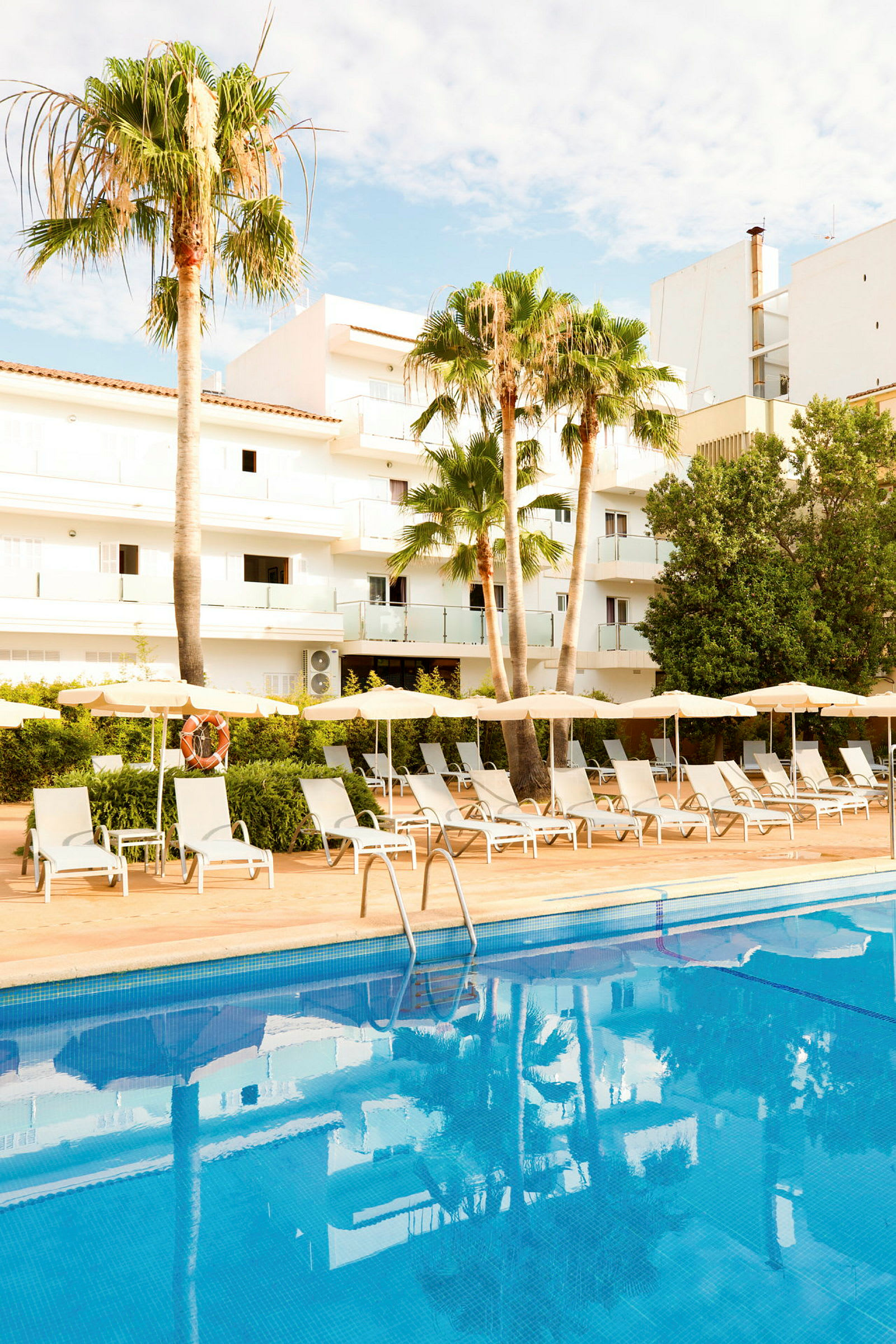 Utomhuspool med solstolar och parasoller på en hotellanläggning med palmer. (AI-genererad text)
