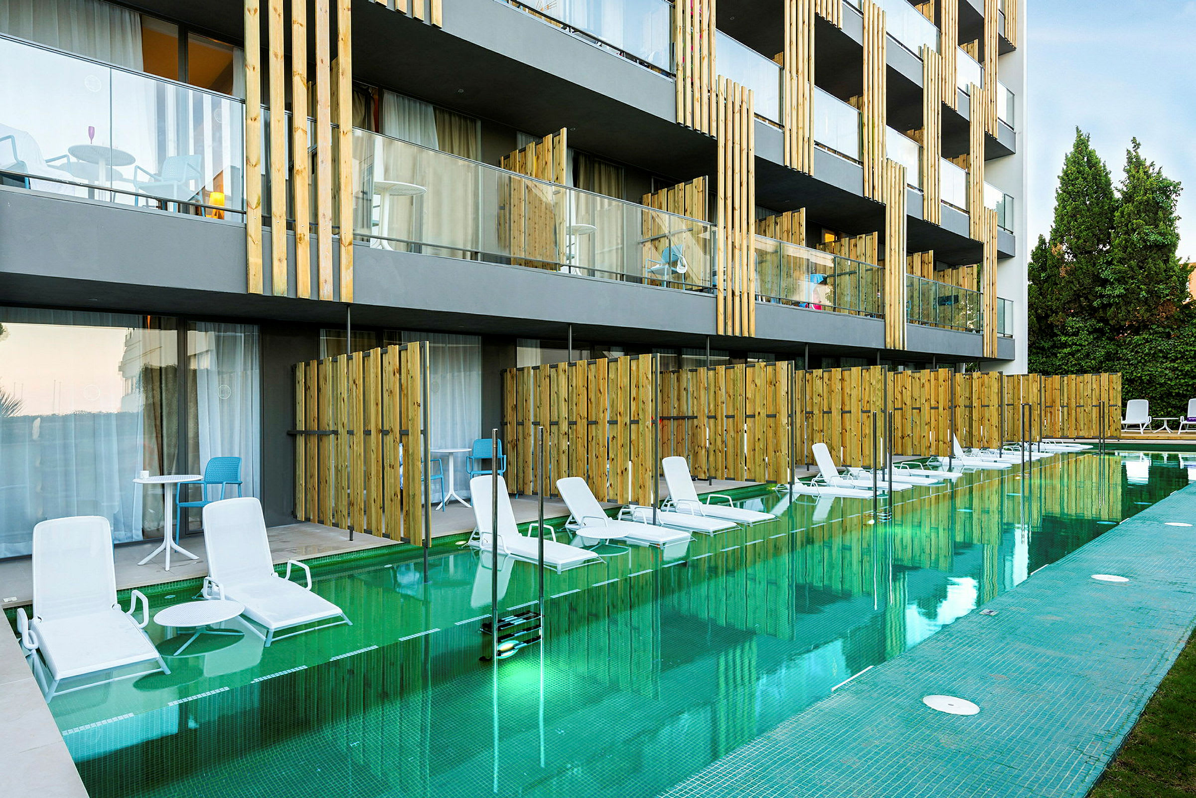 Bild av ett hotell med direkt tillgång till pool från vissa rum. Solstolar står vid poolkanten. (AI-genererad text)