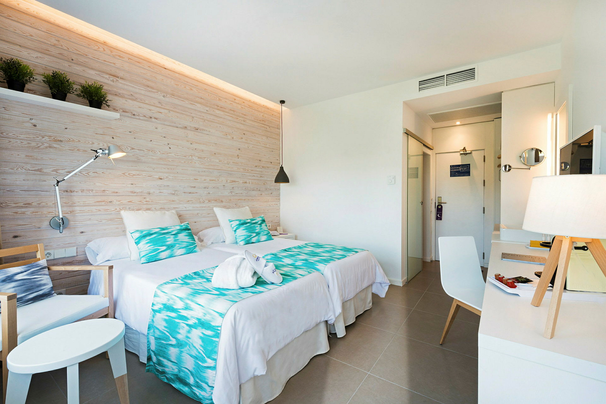 Ett hotellrum med två sängar, en skrivbord och stol samt en dekorativ vägg. (AI-genererad text)