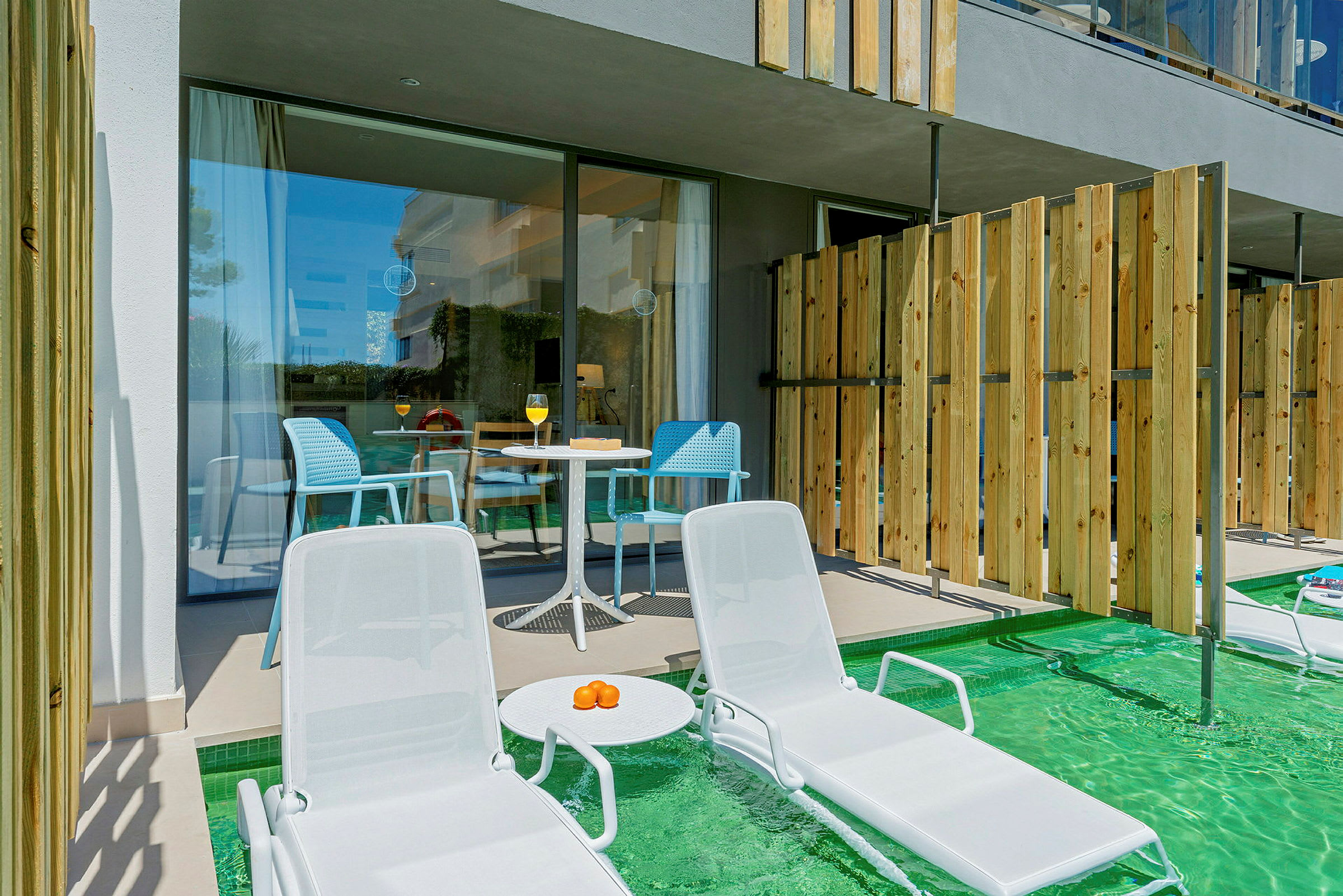 Två solstolar vid en pool med en terrass och bord i bakgrunden. (AI-genererad text)