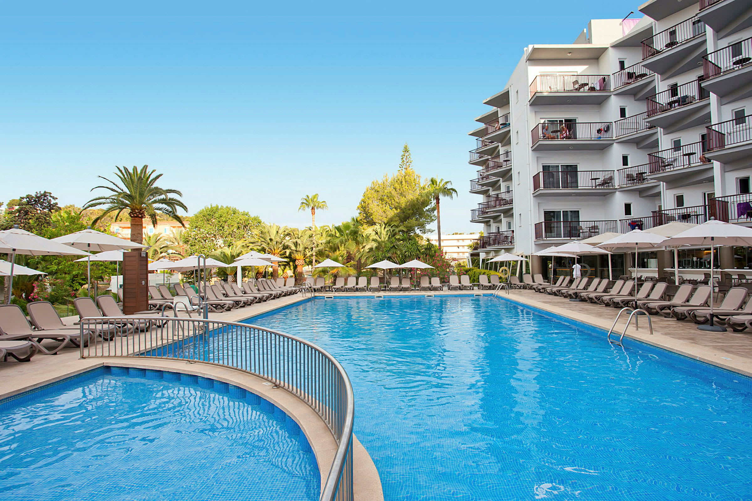 Stor pool omgiven av solstolar och parasoller vid ett hotell. (AI-genererad text)