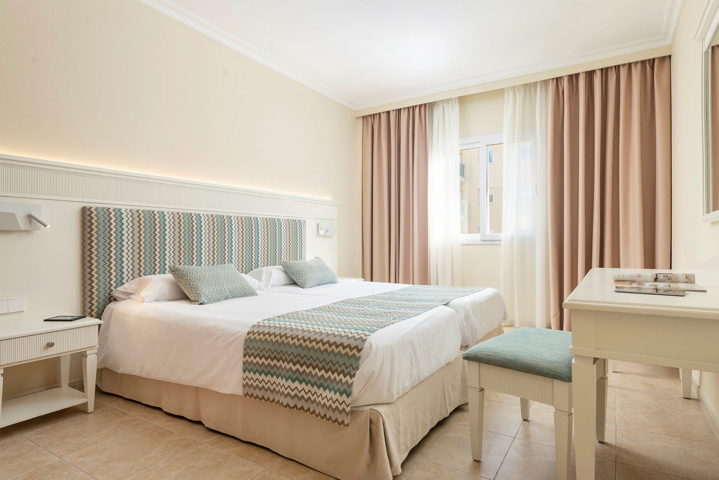 Hotellrum med en dubbelsäng, ljusa färger och ett fönster med gardiner. (AI-genererad text)