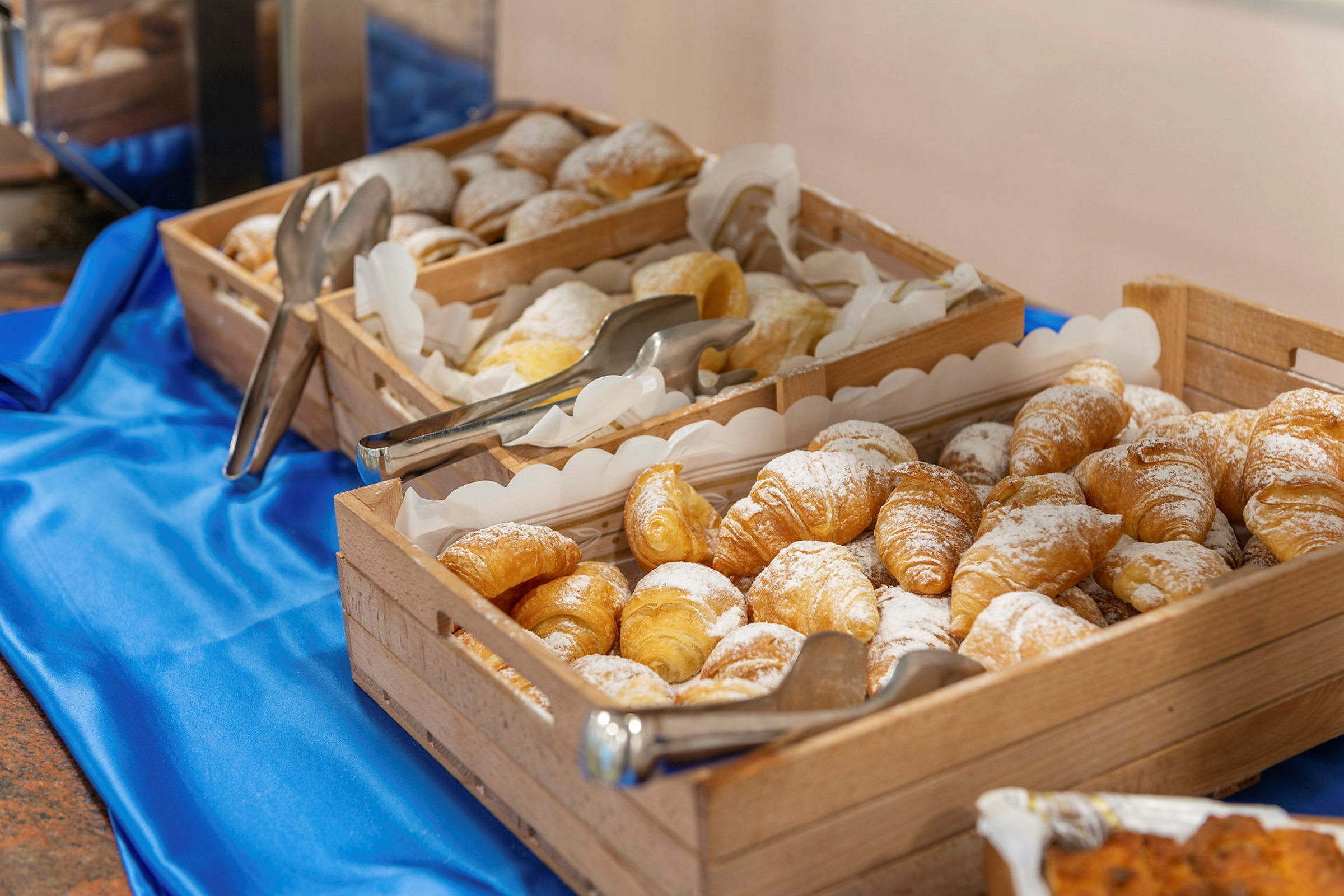 Träkorgar fyllda med croissanter, beströdda med florsocker, på en blå duk. (AI-genererad text)
