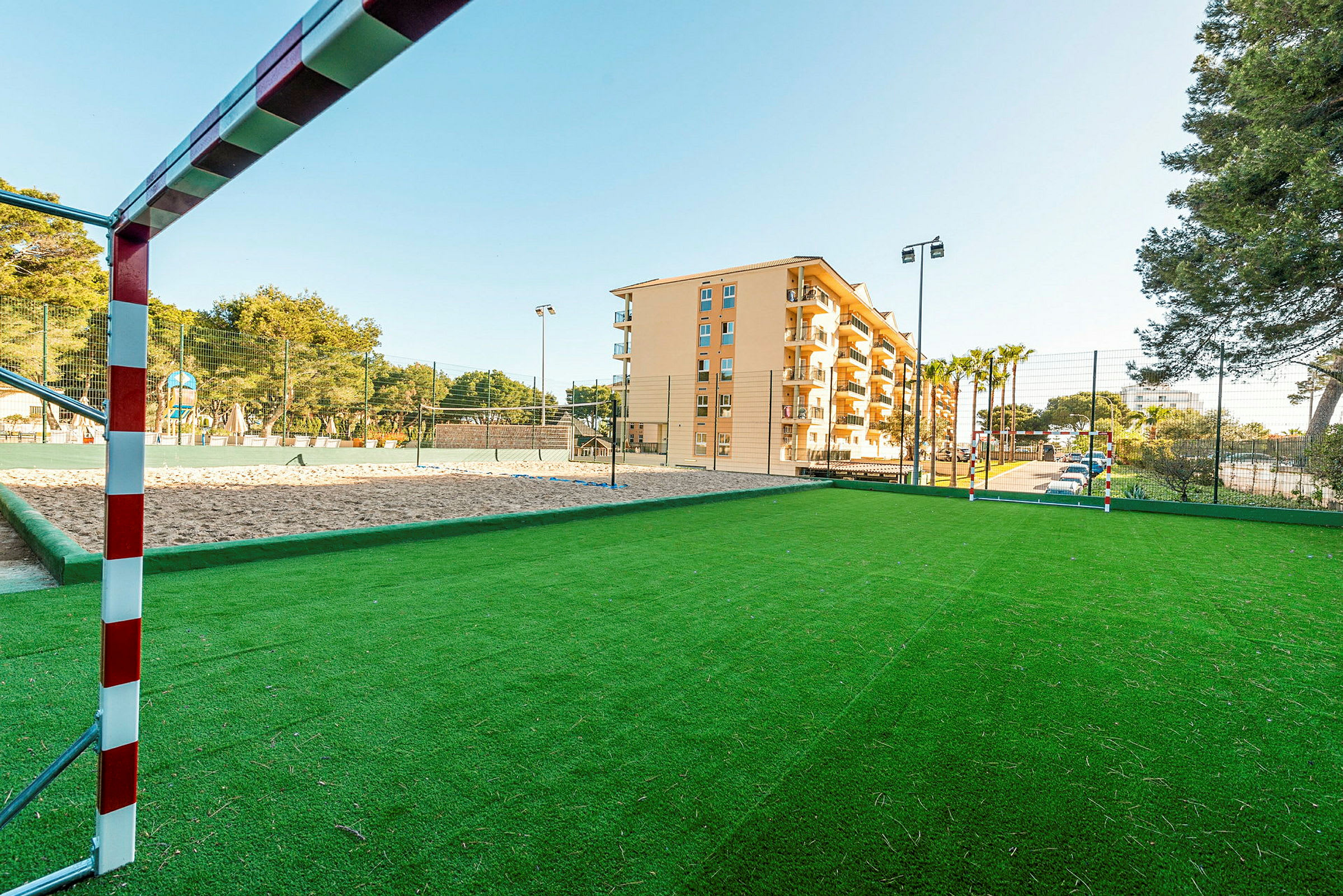 En fotbollsplan med gräs och ett mål i förgrunden samt en byggnad i bakgrunden. (AI-genererad text)