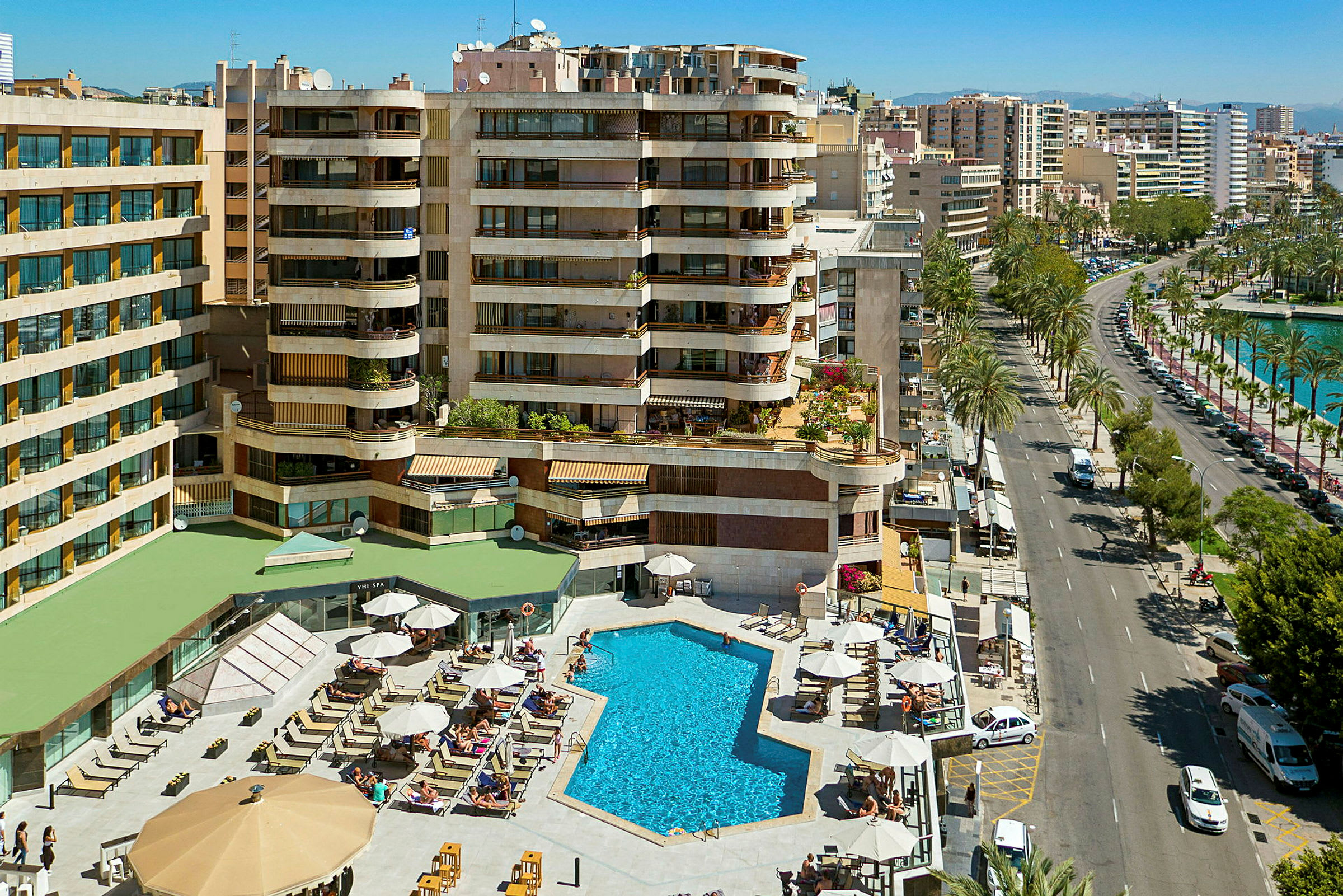 Ett hotellområde med pool och solstolar vid en stadsgata. (AI-genererad text)