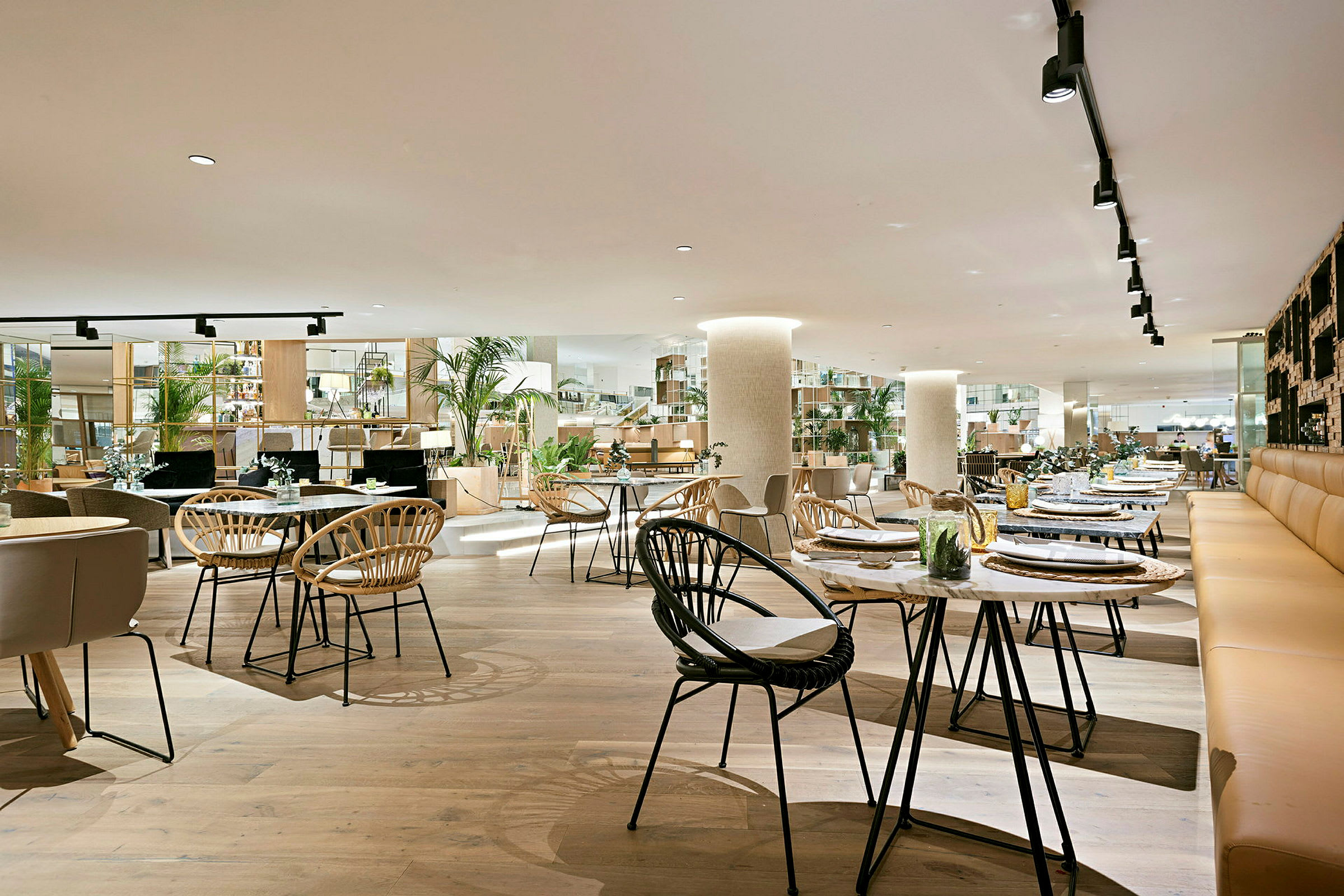 En rymlig restaurang med modern inredning, träbord och stolar samt gröna växter som dekoration. (AI-genererad text)