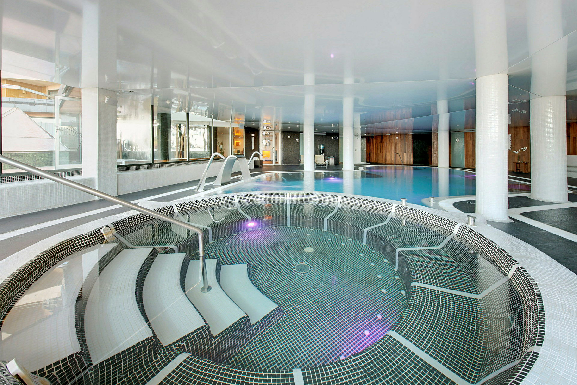 En inomhuspool med en bubbelpool i förgrunden och en större pool i bakgrunden. (AI-genererad text)