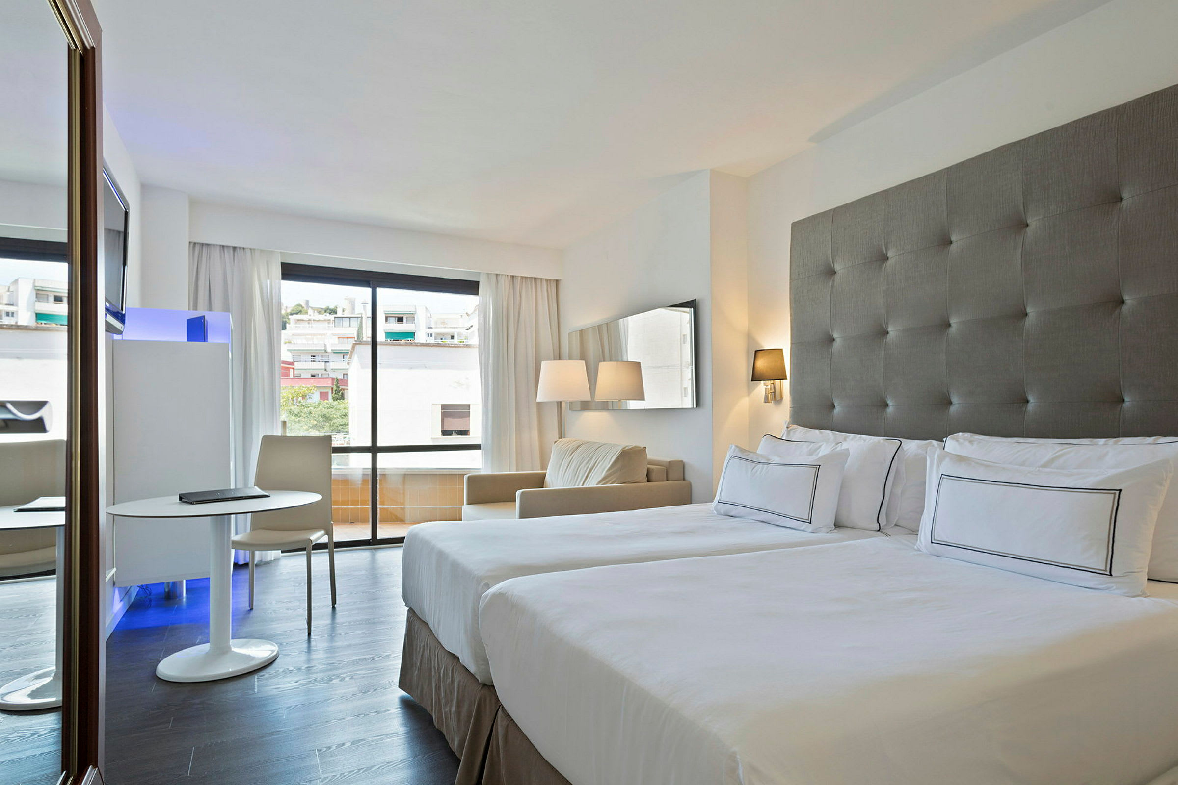 Hotel rum med två sängar, ett fönster som vetter mot staden och en sittgrupp med ett bord och stol. (AI-genererad text)