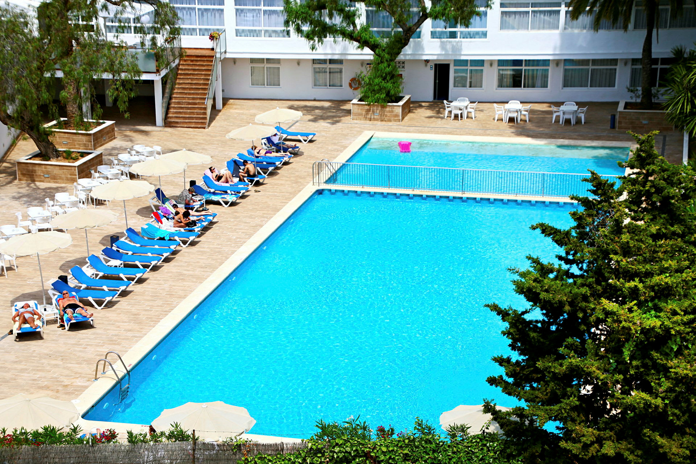En hotellpool med solstolar, parasoller och människor som njuter av solen. (AI-genererad text)