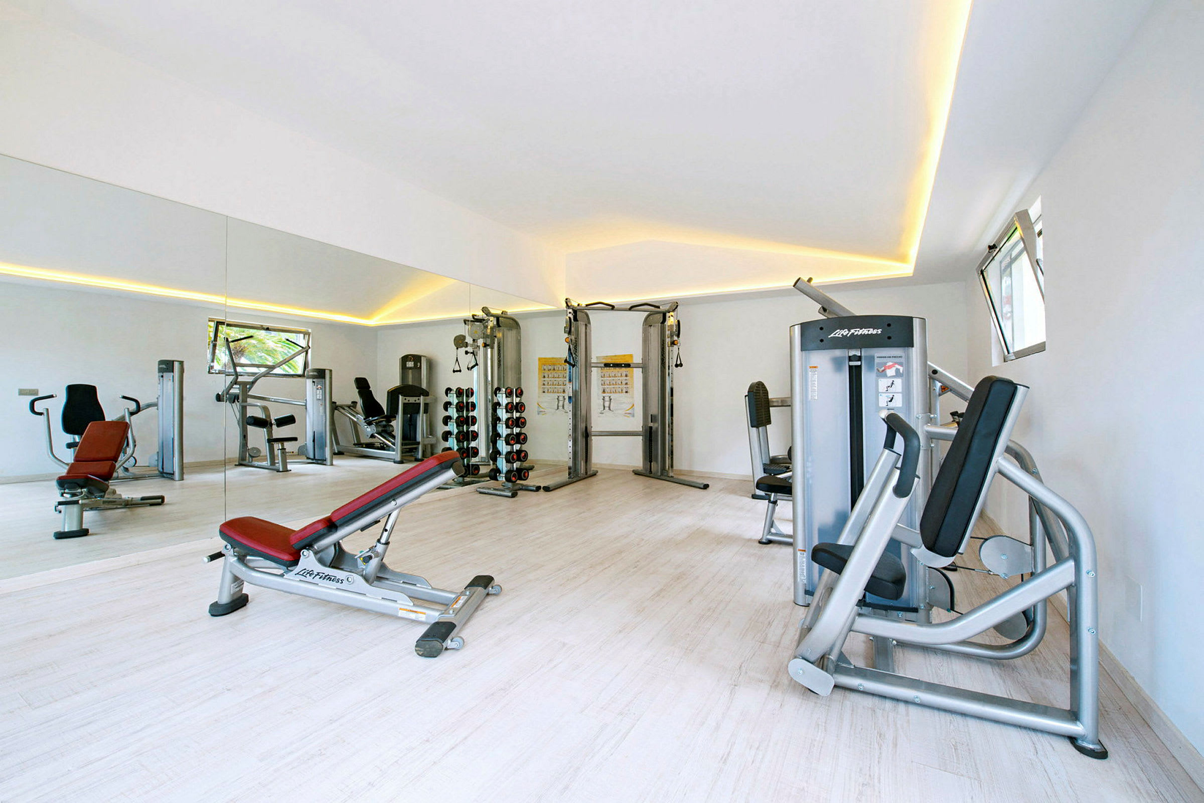 Ett gym med träningsmaskiner, spegelvägg och ljus inredning. (AI-genererad text)