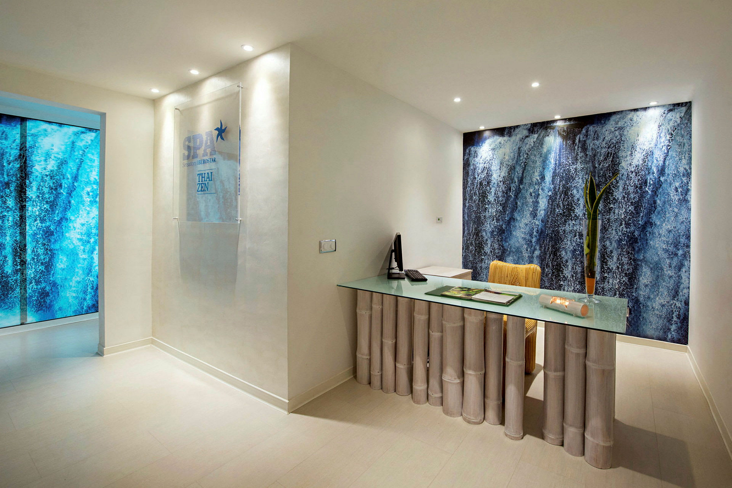 En reception i en spa-anläggning med ett bord av bambu och en bakgrundsvägg med vattenfallsmotiv. (AI-genererad text)