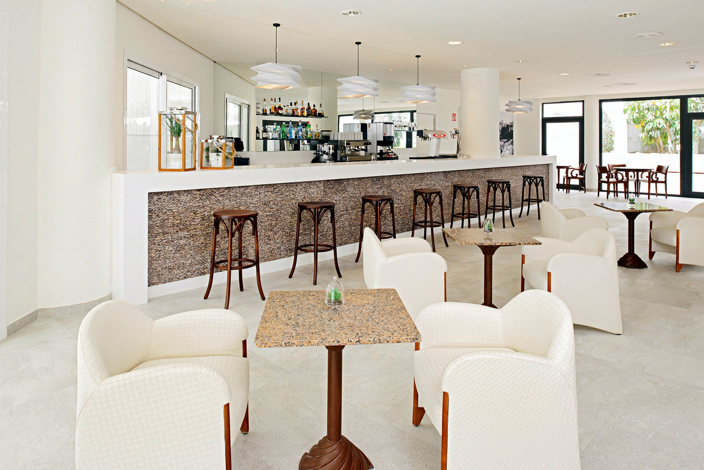Bild på en modern hotellbar med en lång bardisk, höga barstolar och sittgrupper med fåtöljer och små bord. (AI-genererad text)