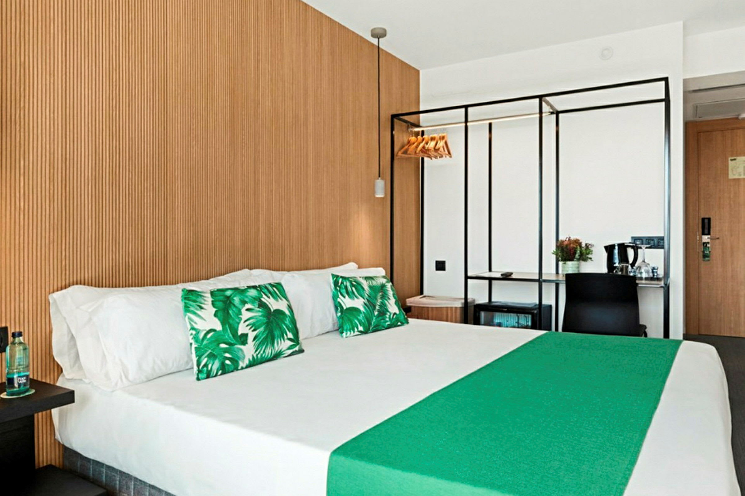Hotellrum med dubbelsäng, gröna dekorationskuddar och träpanel på väggen. (AI-genererad text)