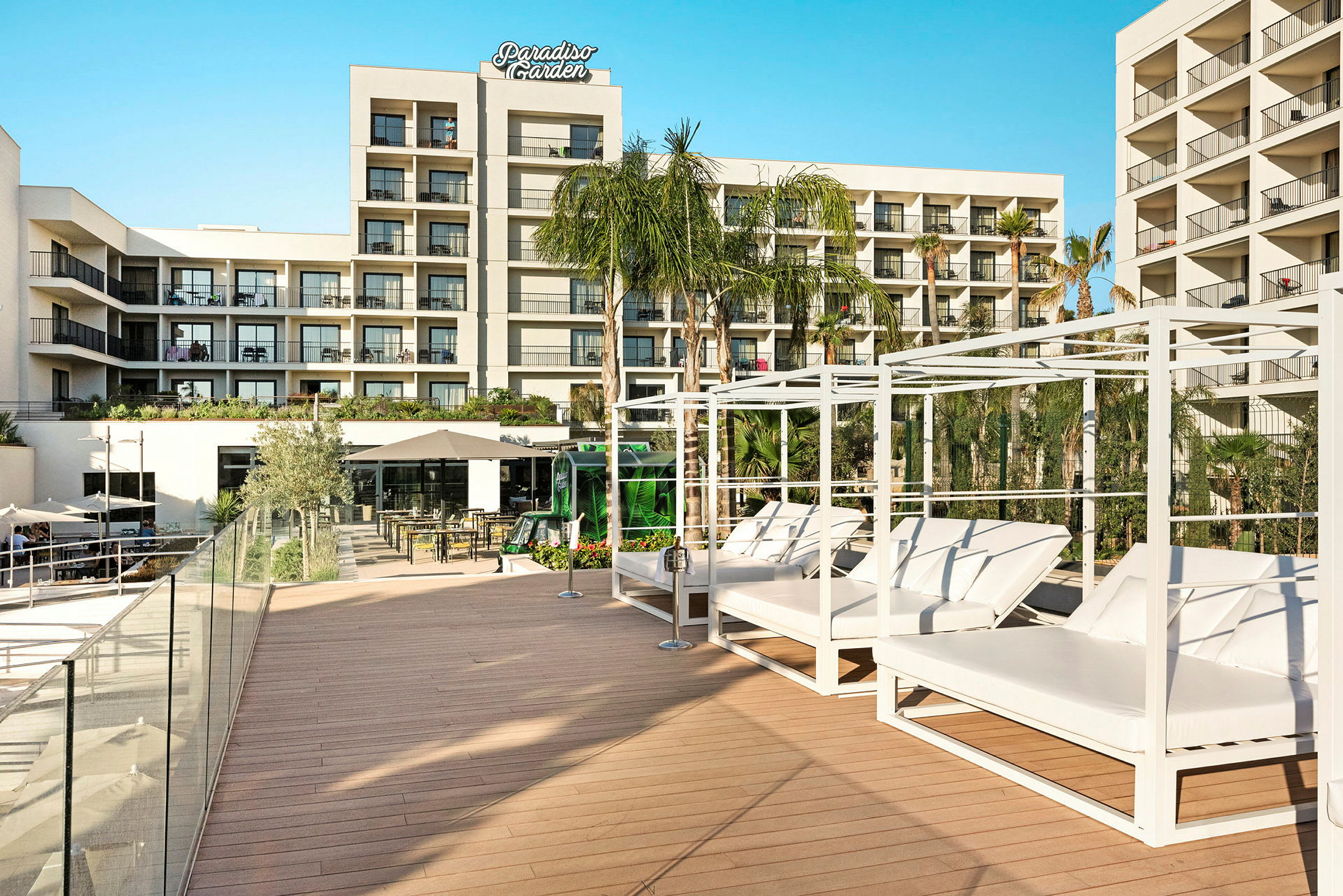 Hotellbyggnad med balkonger och en solterrass med solsängar och palmer. (AI-genererad text)