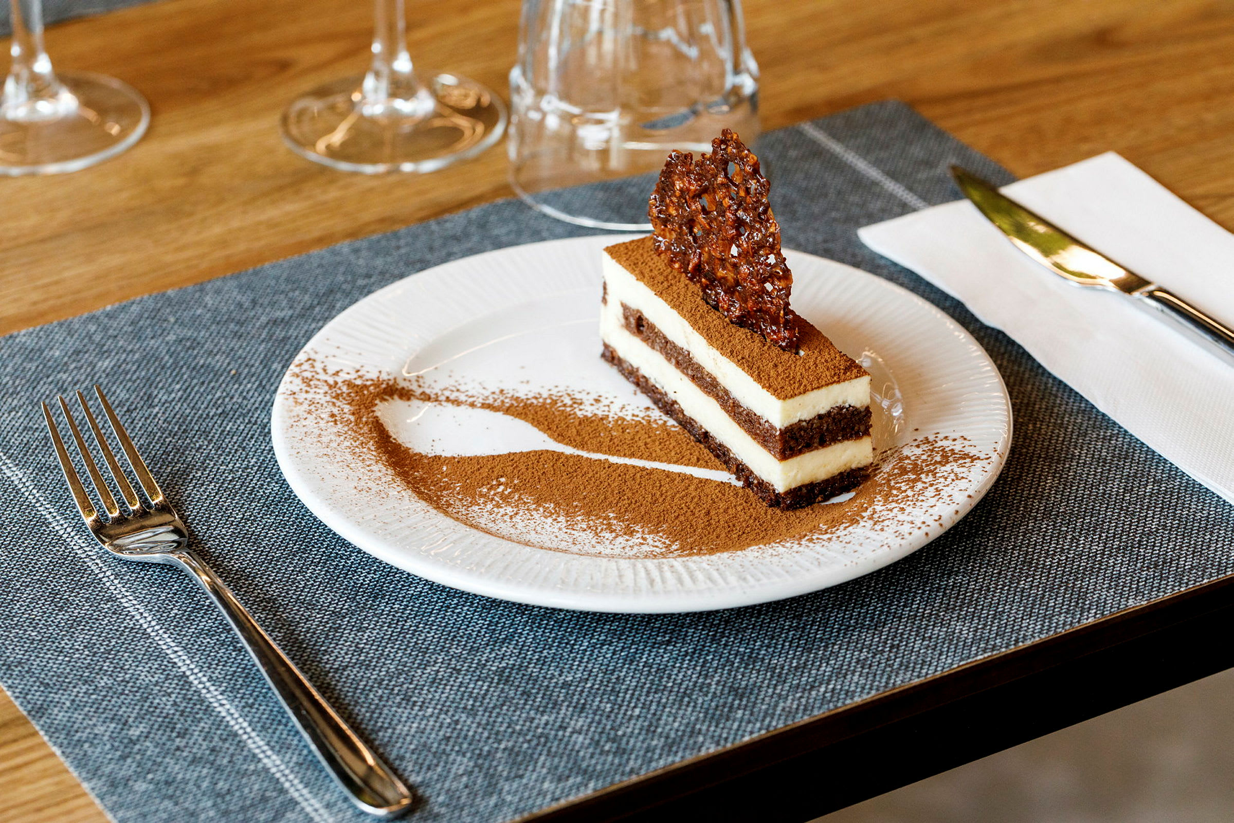 En dessert, troligen en tiramisu, serverad på en tallrik, dekorerad med kakaopulver och ett krispigt stycke karamell ovanpå. (AI-genererad text)