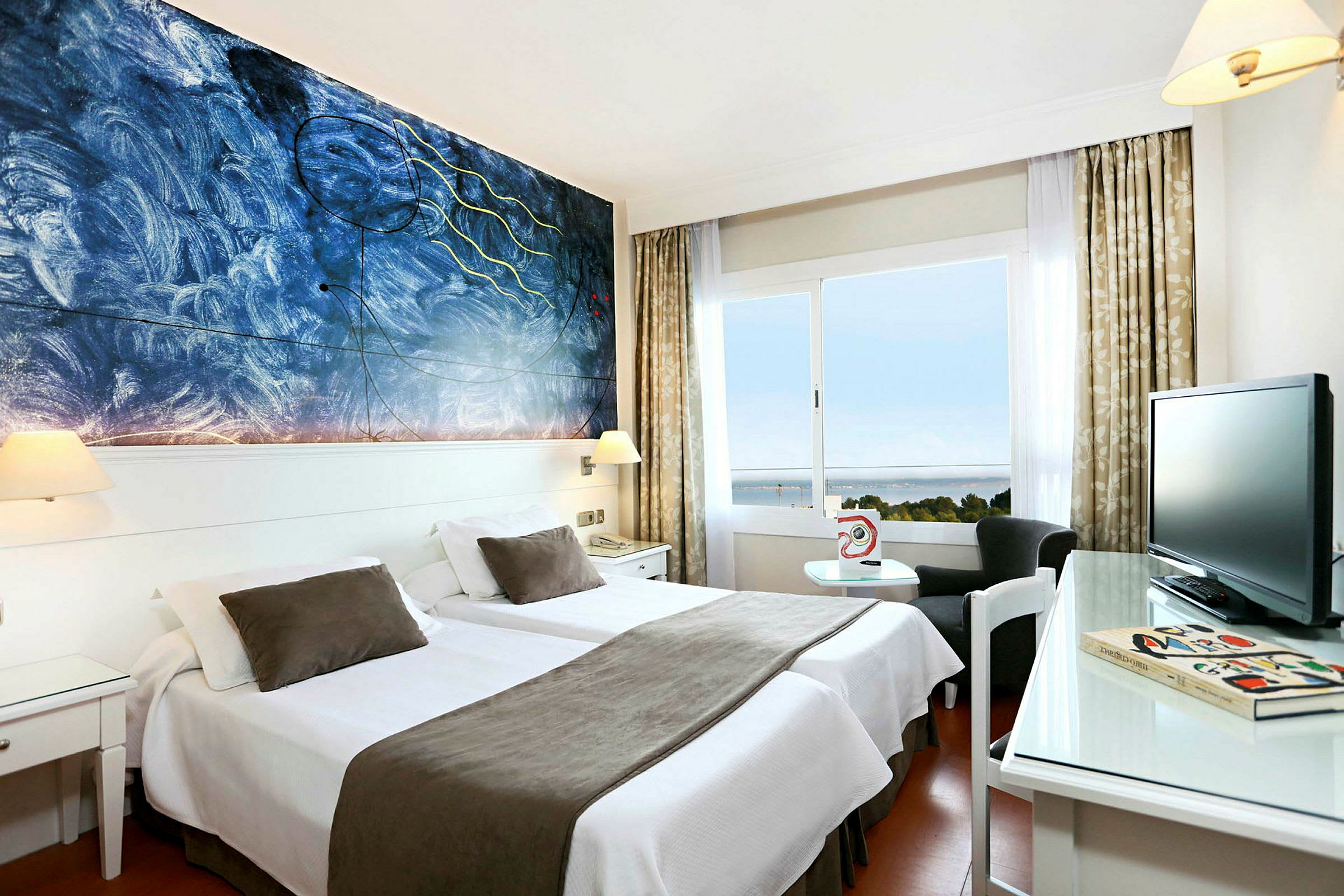 Ett hotellrum med två enkelsängar som har vita sängkläder och bruna överkast, en konstnärlig målning på väggen och ett fönster med utsikt över havet. (AI-genererad text)