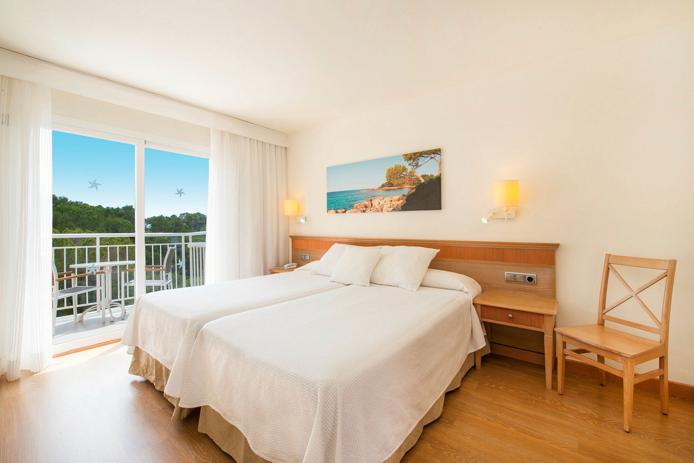 Ett hotellrum med två enkelsängar, en balkong och ett landskapsfoto på väggen. (AI-genererad text)