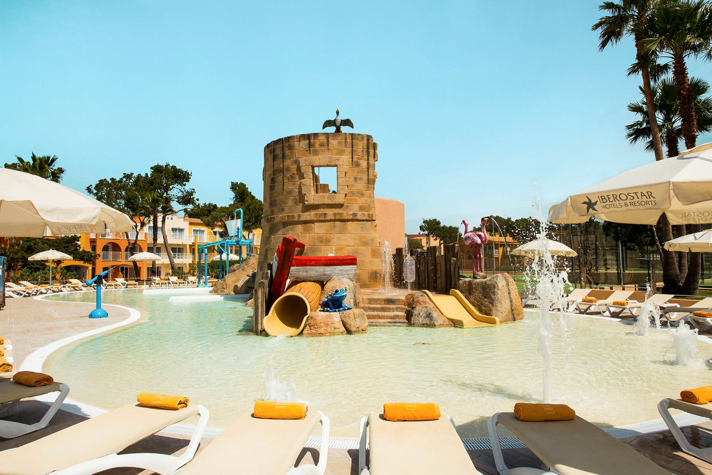 En pool med solstolar, en lekplats med rutschkanor i form av ett torn och färgglada dekorationer. (AI-genererad text)