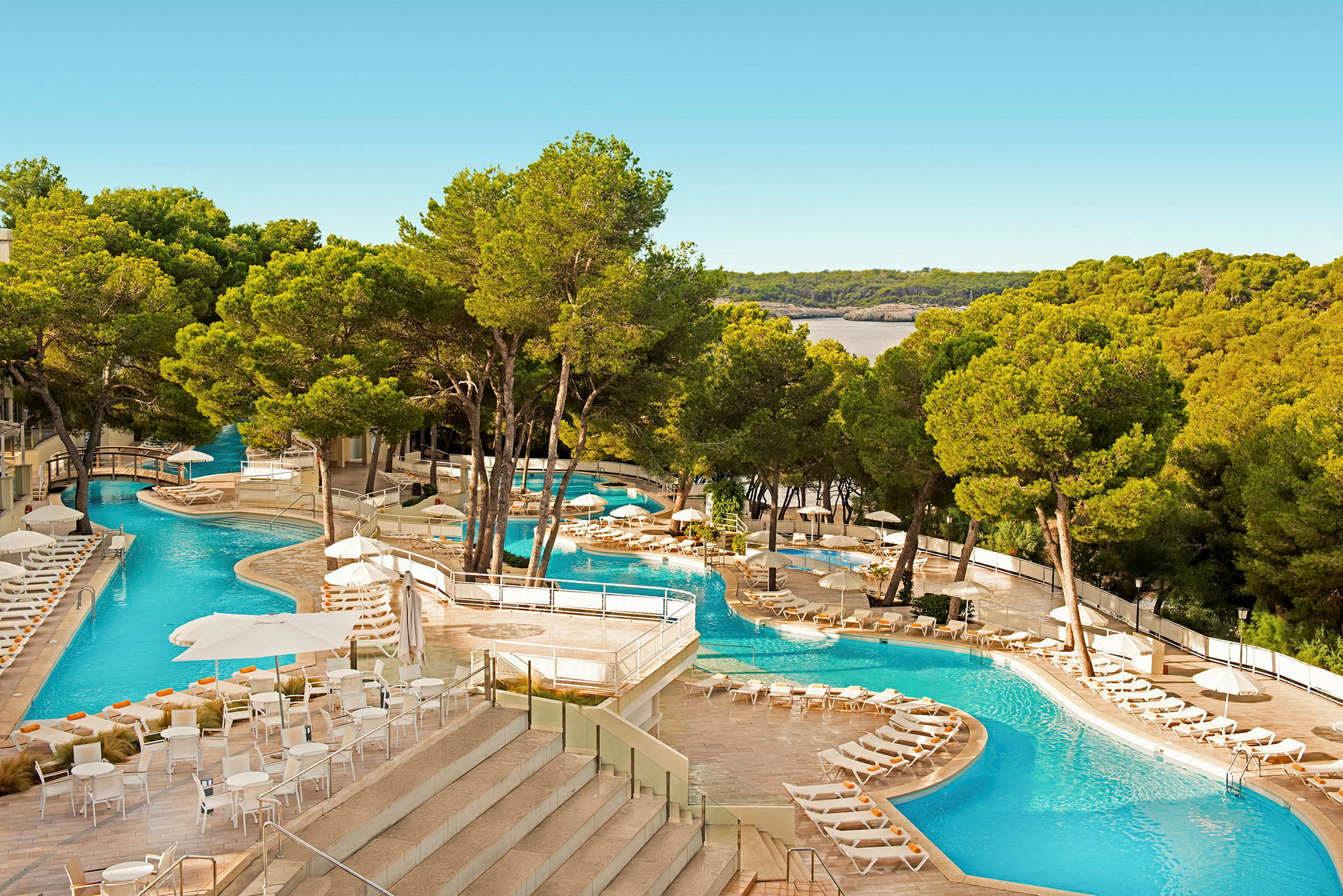 Hotellpool med solstolar omgiven av gröna träd och utsikt över natur. (AI-genererad text)