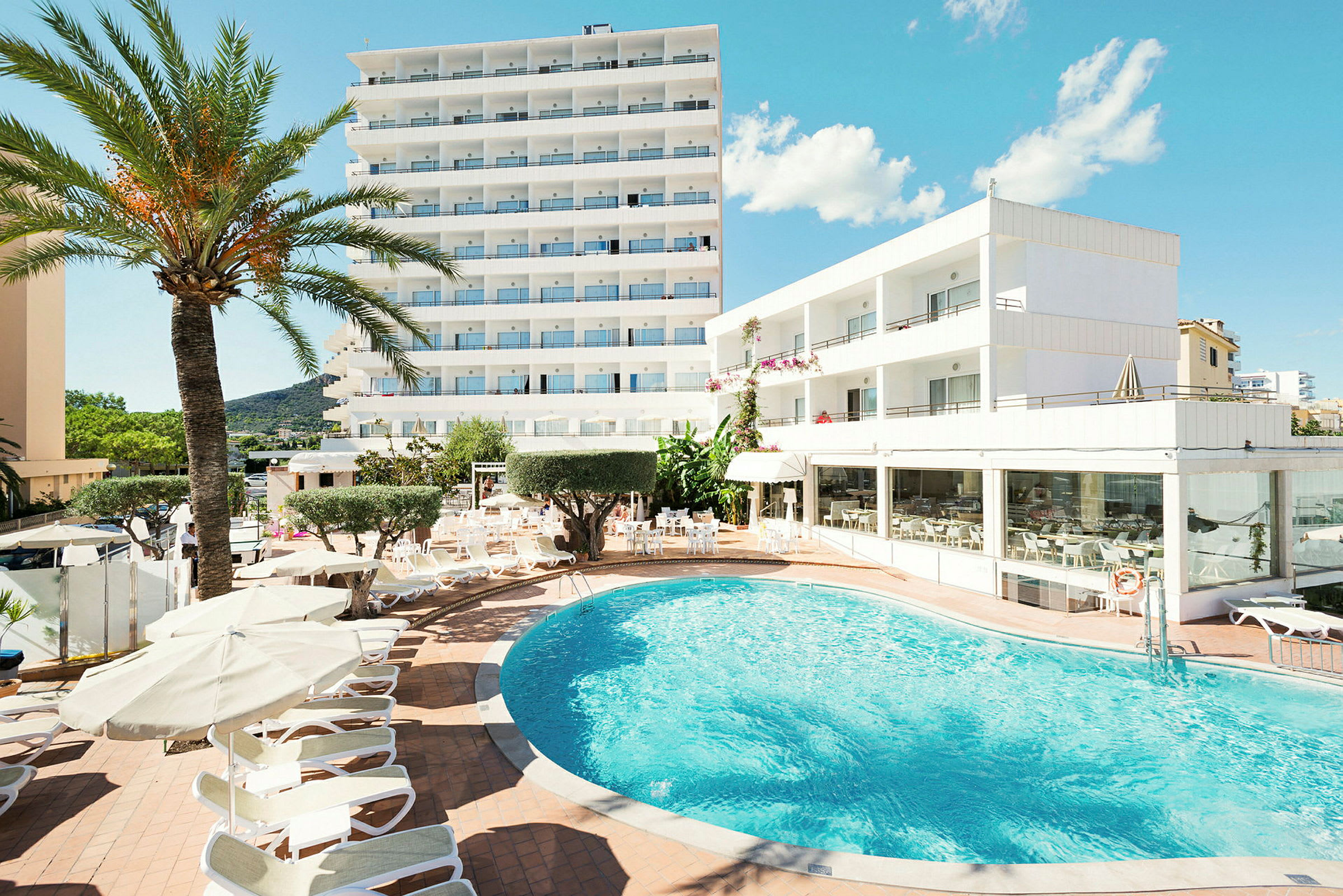 Hotellbyggnader vid en pool med solstolar och parasoller. (AI-genererad text)