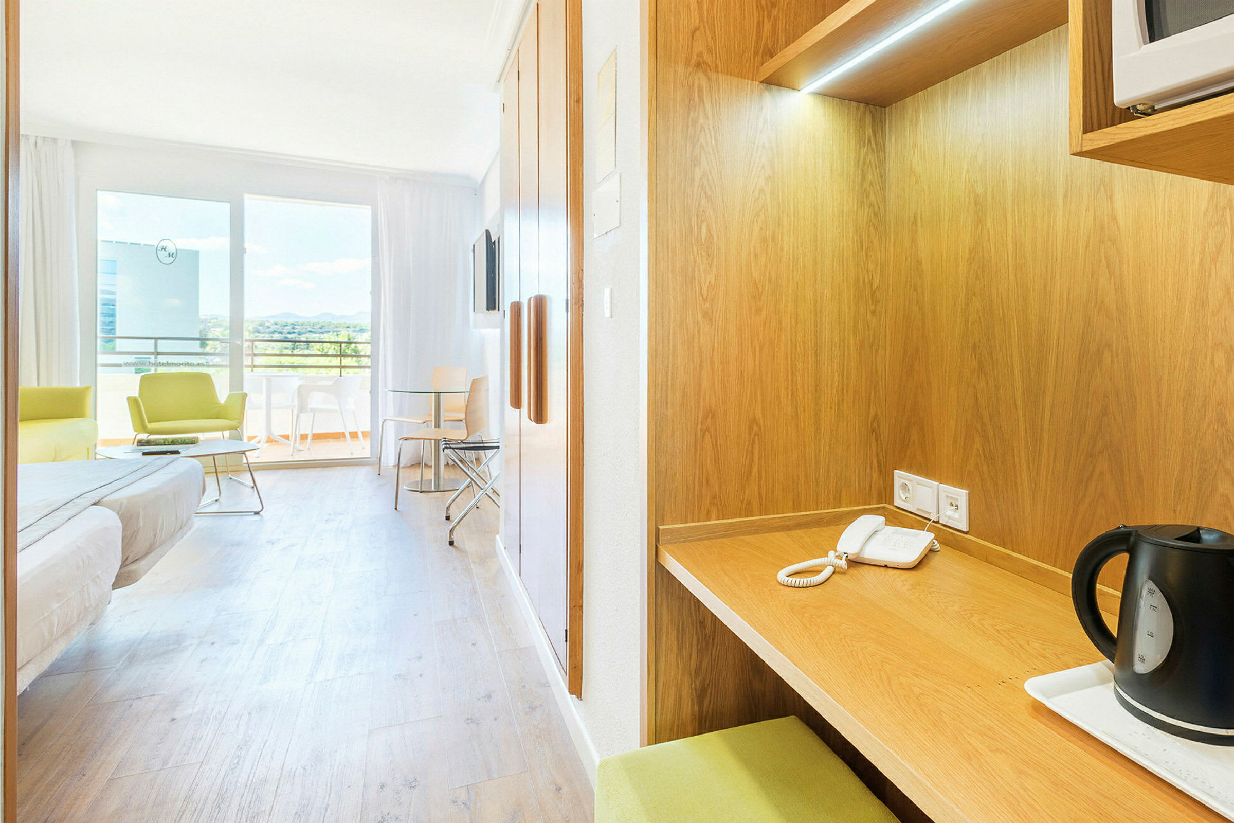 Ett hotellrum med enkelsäng, sittgrupp, skrivbord och bord vid en balkong. (AI-genererad text)