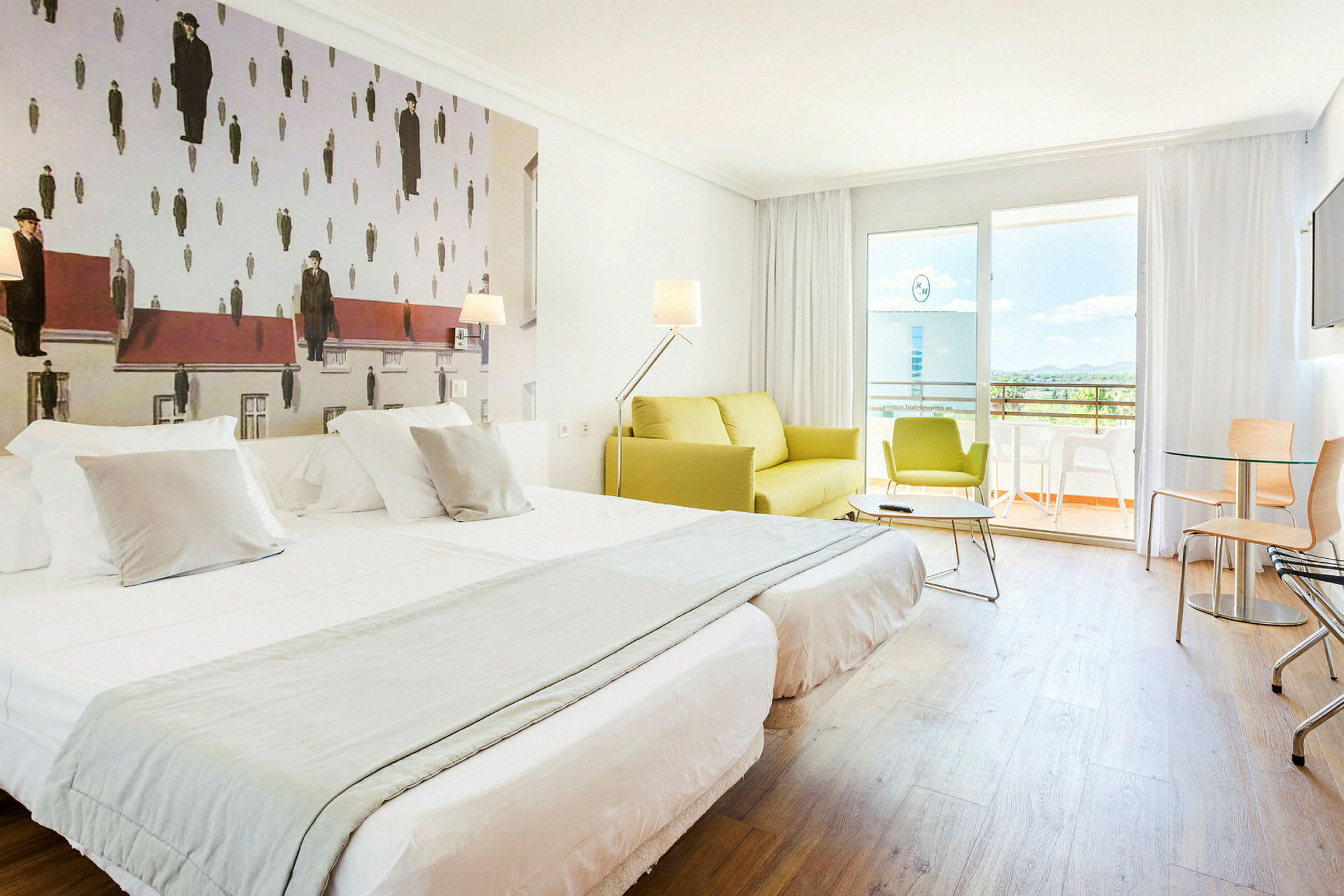 Ett hotellrum med två bäddade enkelsängar, en grön soffa och en balkong i bakgrunden. Väggdekorationen har ett konstverk med en ovanlig design. (AI-genererad text)